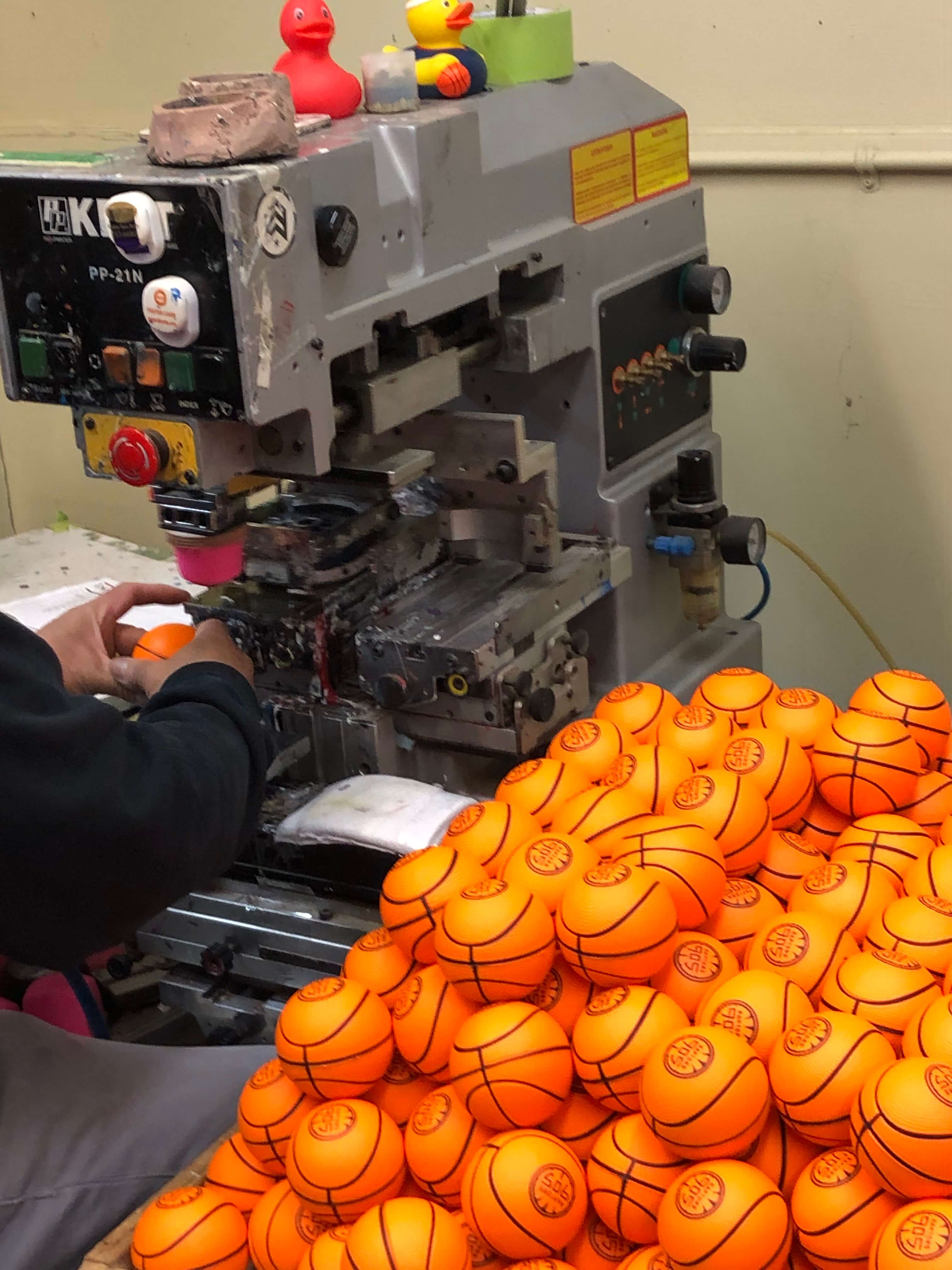 Pile of miniature rubber basketballs sitting next to pad printing machinery. 