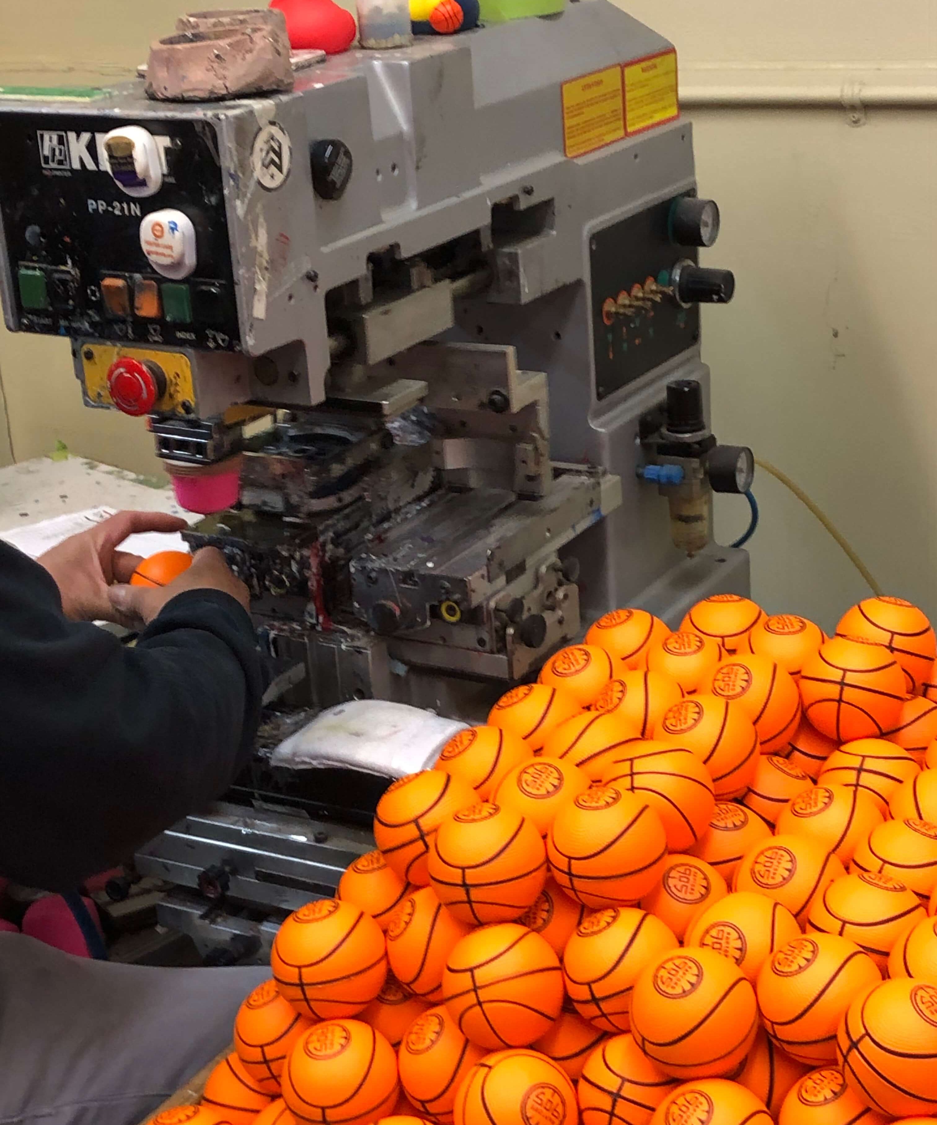 Pile of miniature rubber basketballs sitting next to pad printing machinery.