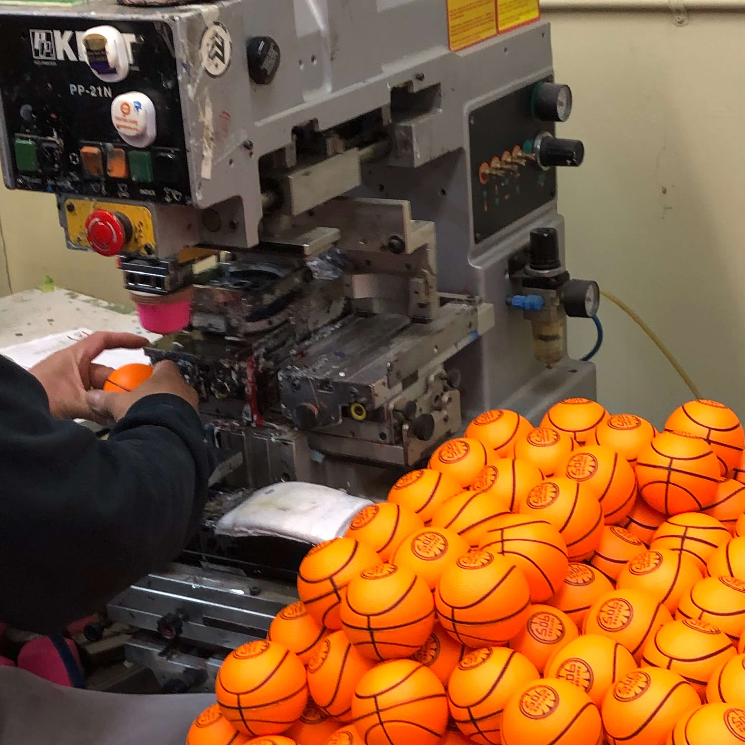 Pile of miniature rubber basketballs sitting next to pad printing machinery.