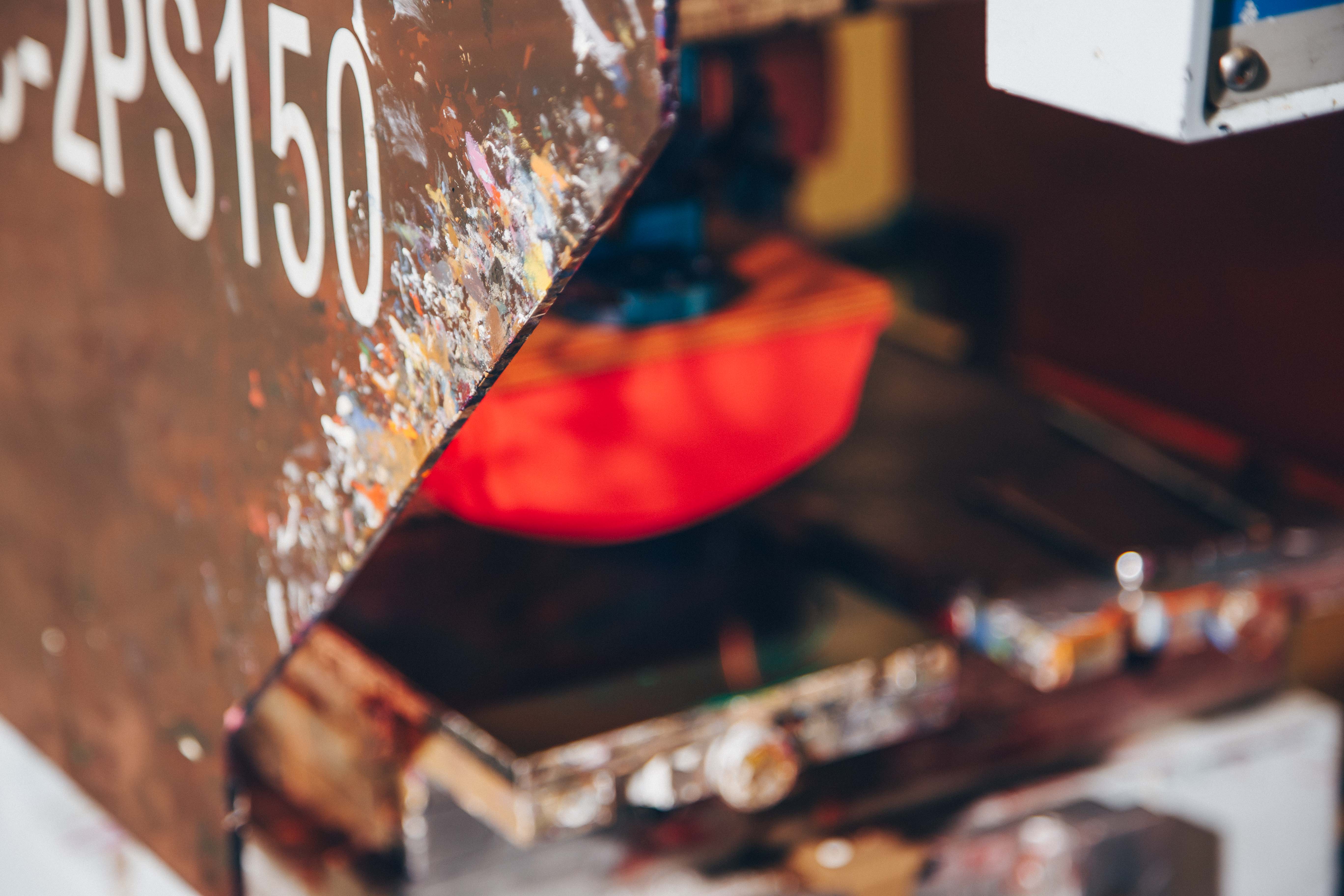 A close-up of a paint-splattered pad printing machine, used for precision printing on products. The machine's vibrant colors and well-used appearance highlight its role in creating detailed custom prints on various surfaces.
