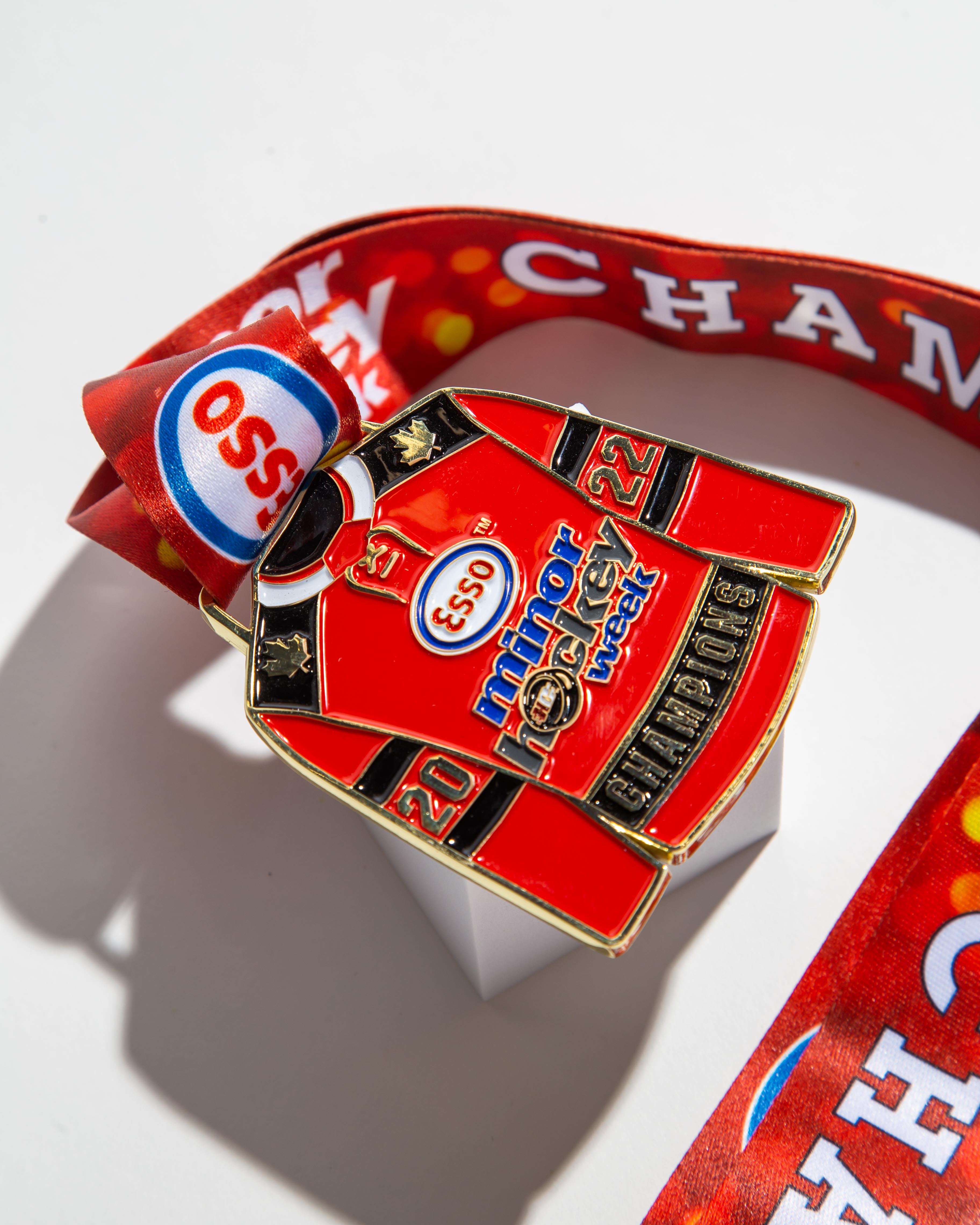 Unique hockey jersey-shaped medal for Esso Minor Hockey Week 2022 Champions, customized with vibrant red ribbon and detailed engraving.