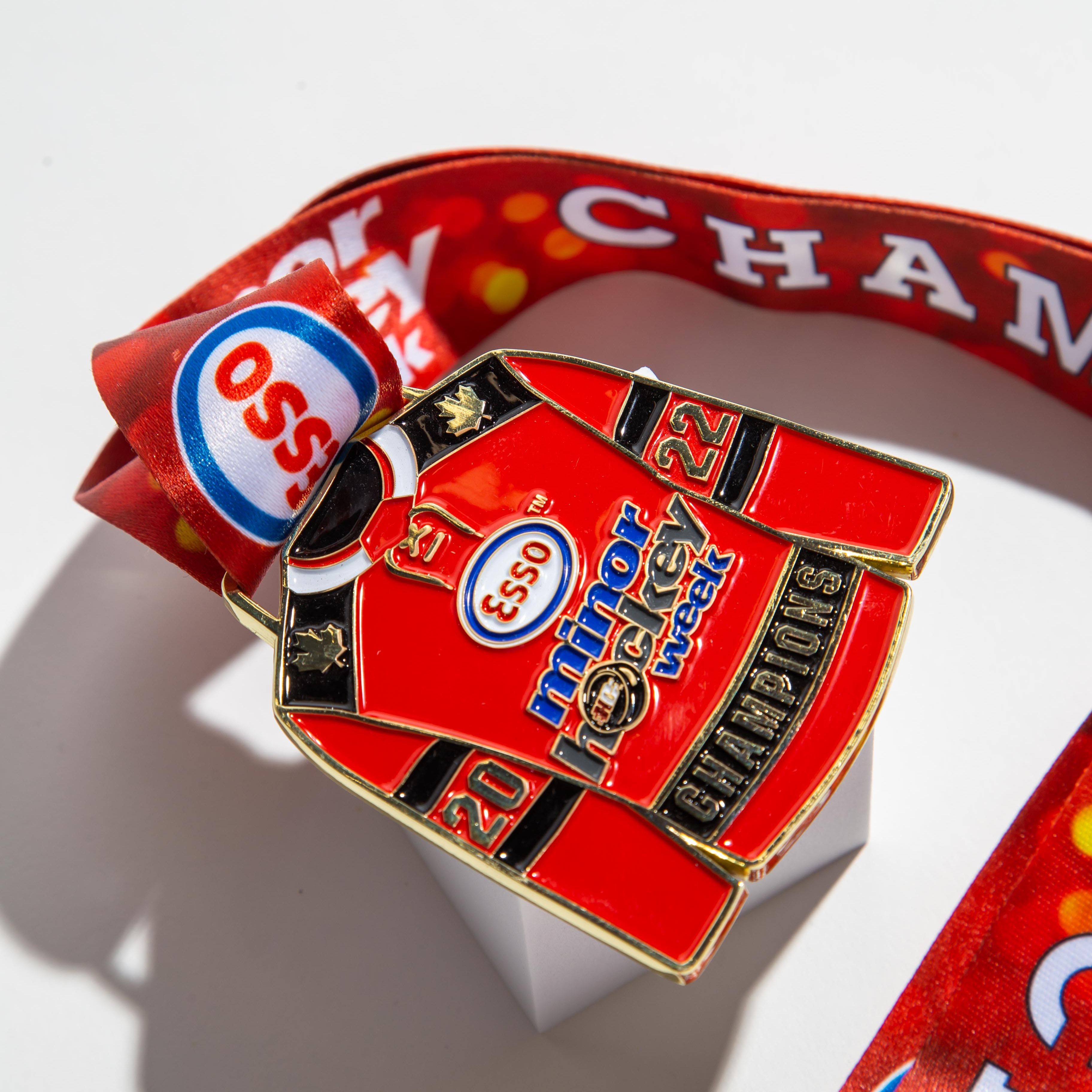 Unique hockey jersey-shaped medal for Esso Minor Hockey Week 2022 Champions, customized with vibrant red ribbon and detailed engraving.