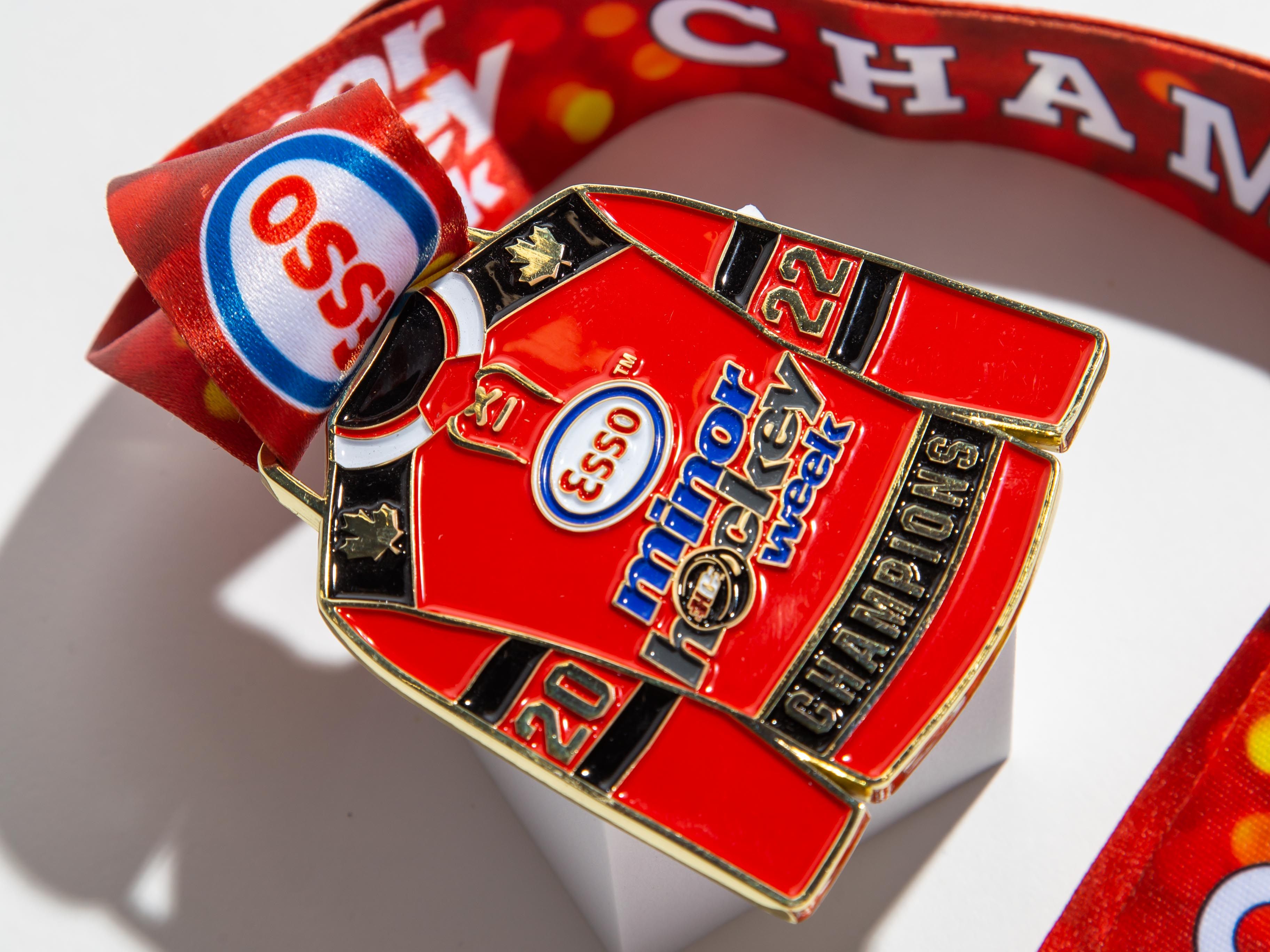 Unique hockey jersey-shaped medal for Esso Minor Hockey Week 2022 Champions, customized with vibrant red ribbon and detailed engraving.