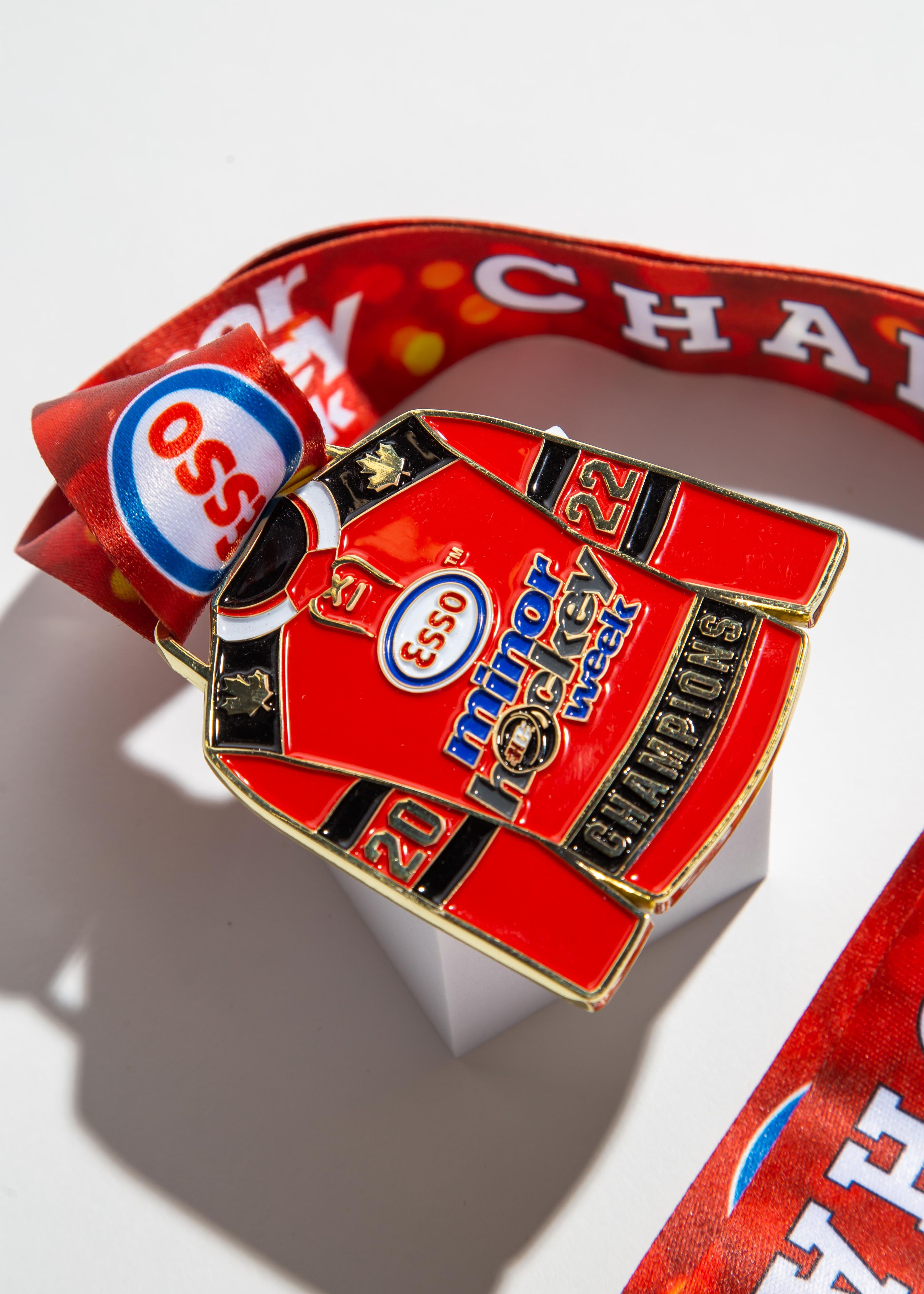 Unique hockey jersey-shaped medal for Esso Minor Hockey Week 2022 Champions, customized with vibrant red ribbon and detailed engraving.