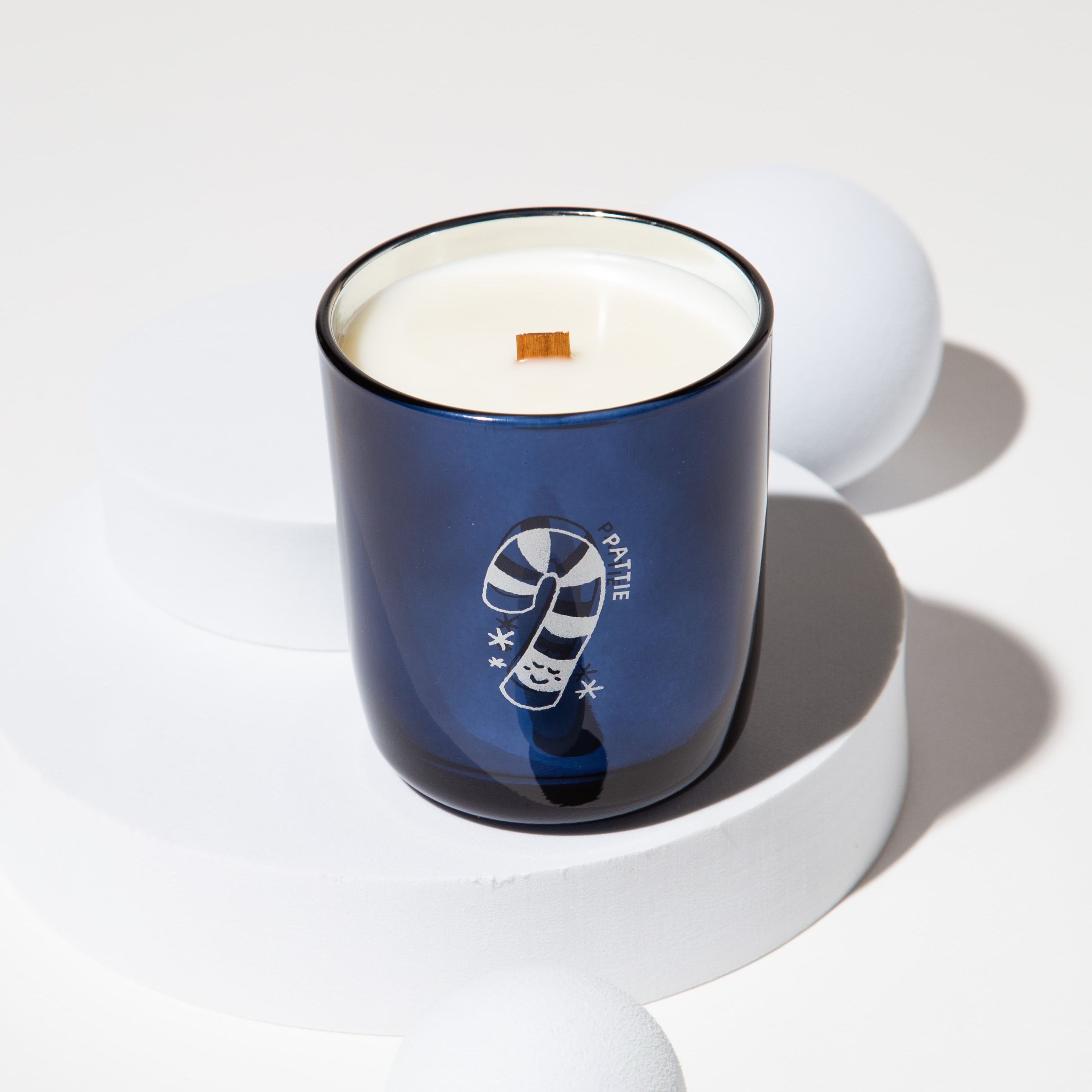 Blue Milk Jar Candle Co branded candle with a wooden wick on a white pedestal, surrounded by white spheres.