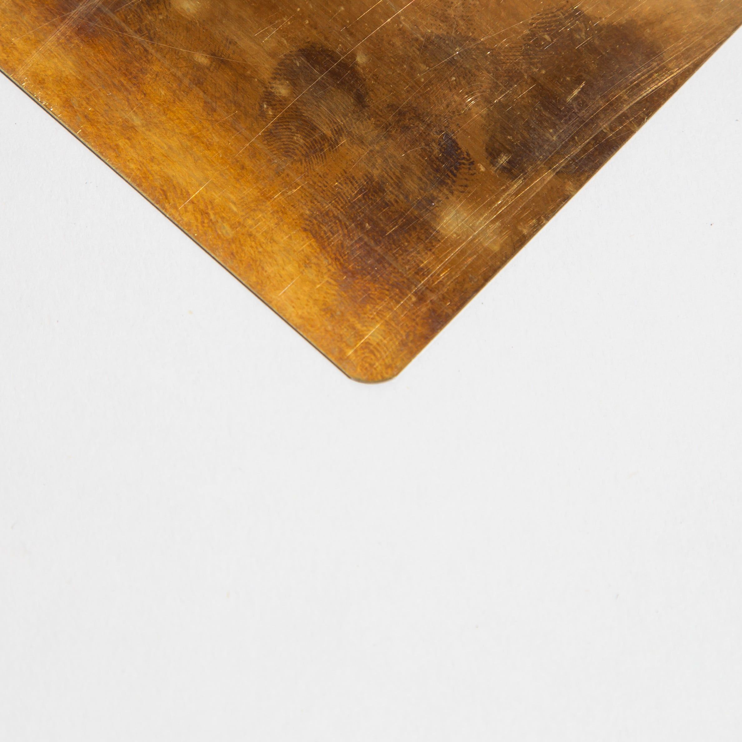 Corner of a scratched, aged metal sheet with a golden-brown patina on a white background.
