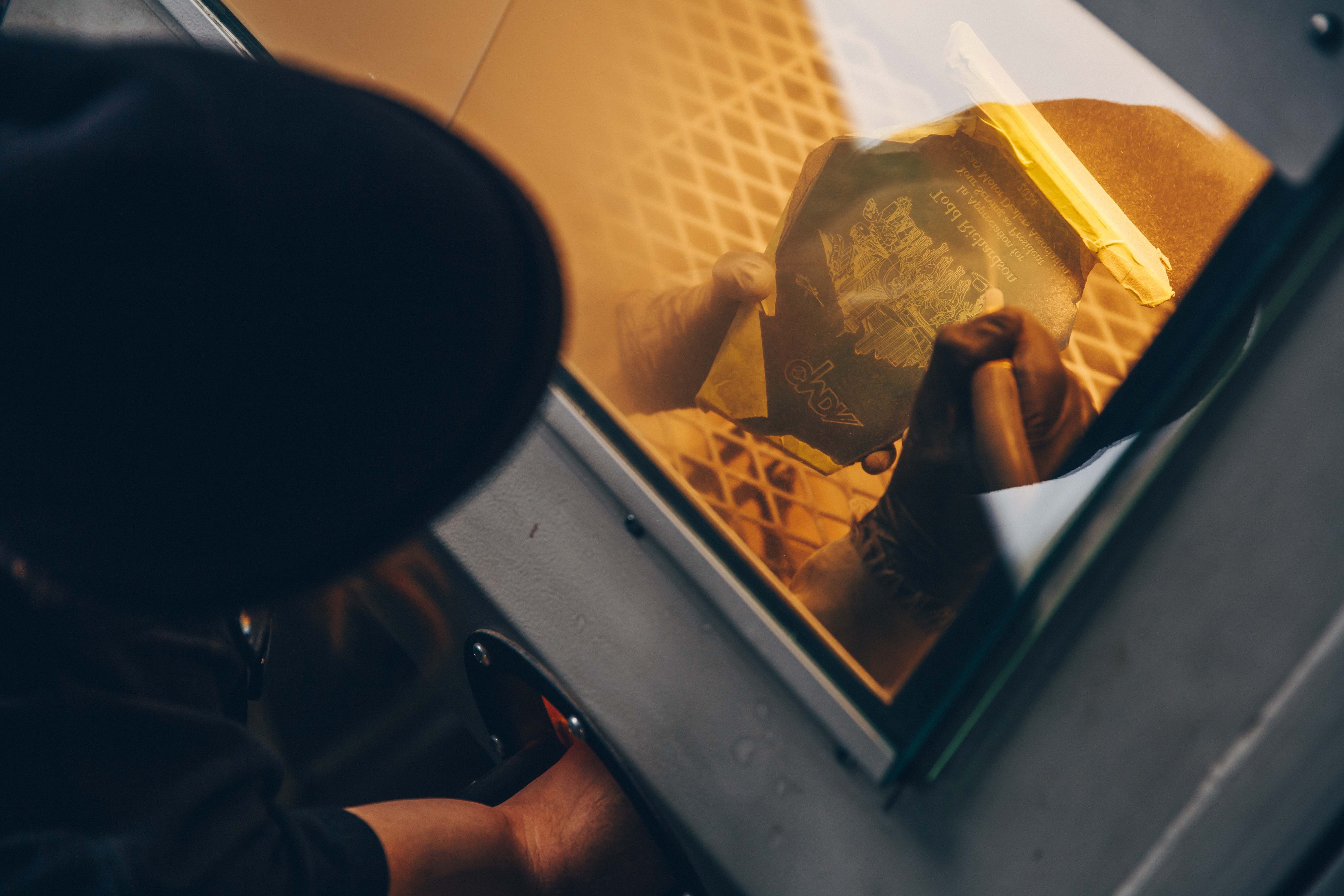 Close-up of a person holding a glass award with intricate engraved details, viewed through the protective window of a sandblasting cabinet.