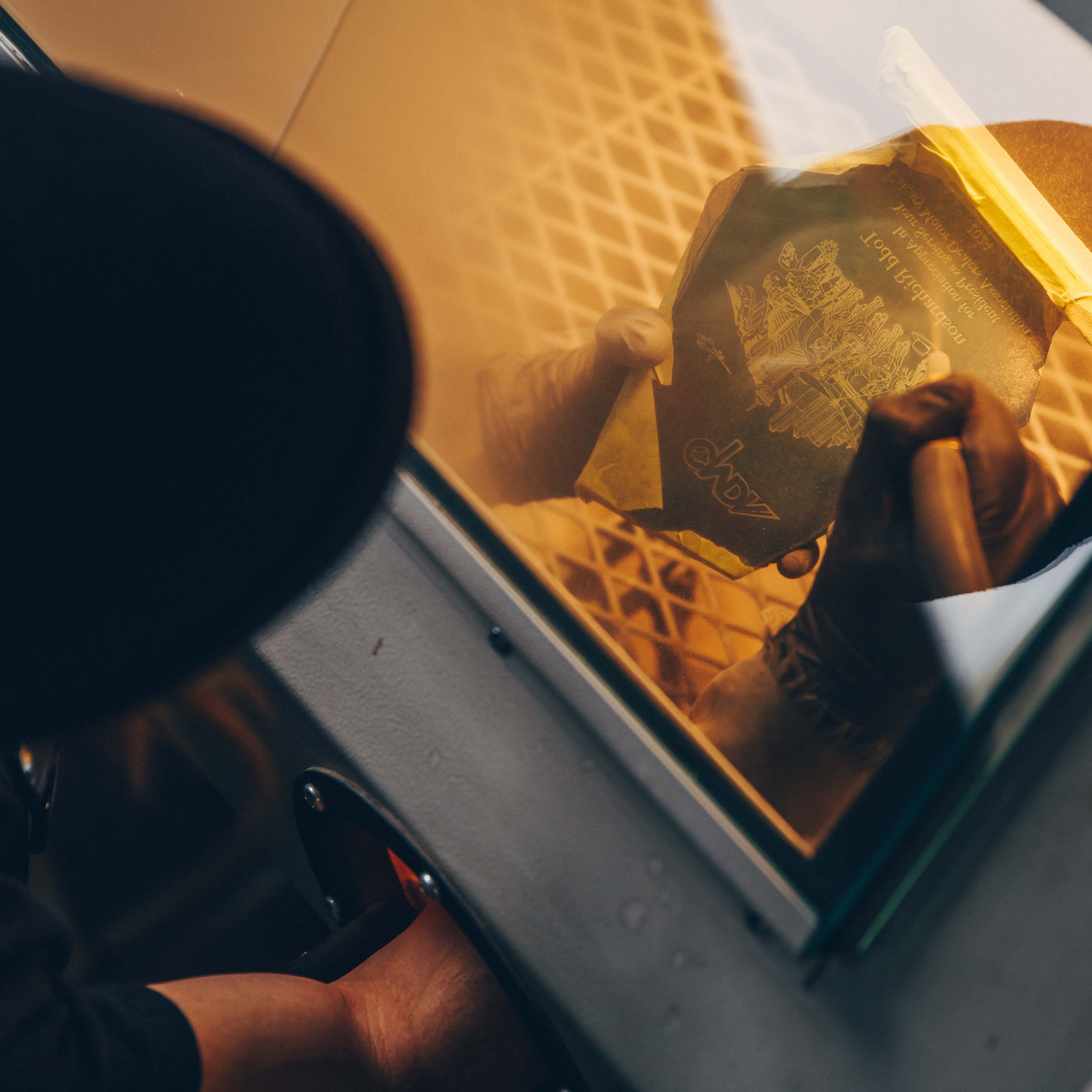 Close-up of a person holding a glass award with intricate engraved details, viewed through the protective window of a sandblasting cabinet.