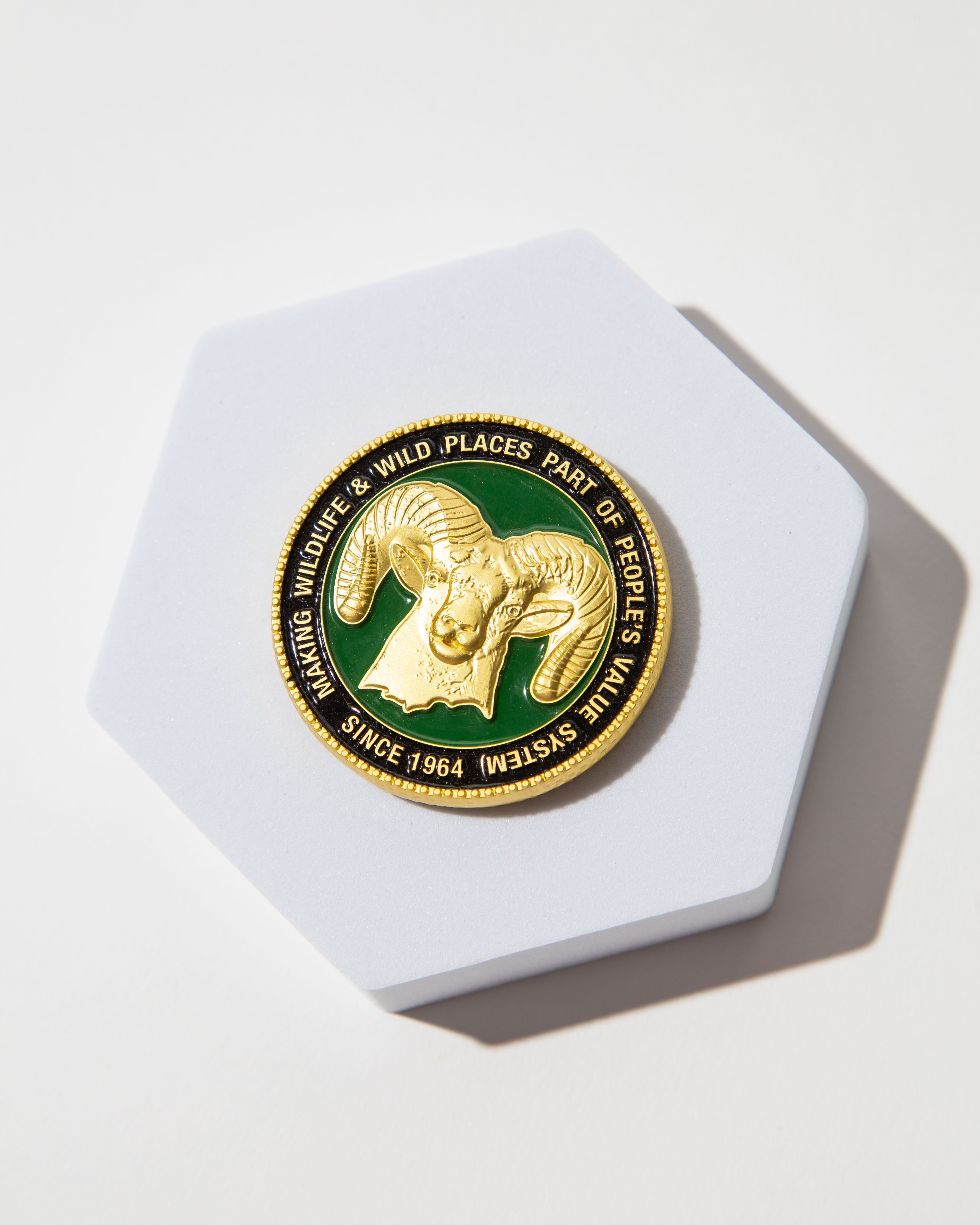 Gold medallion with a ram's head on a green background, promoting wildlife conservation since 1964.