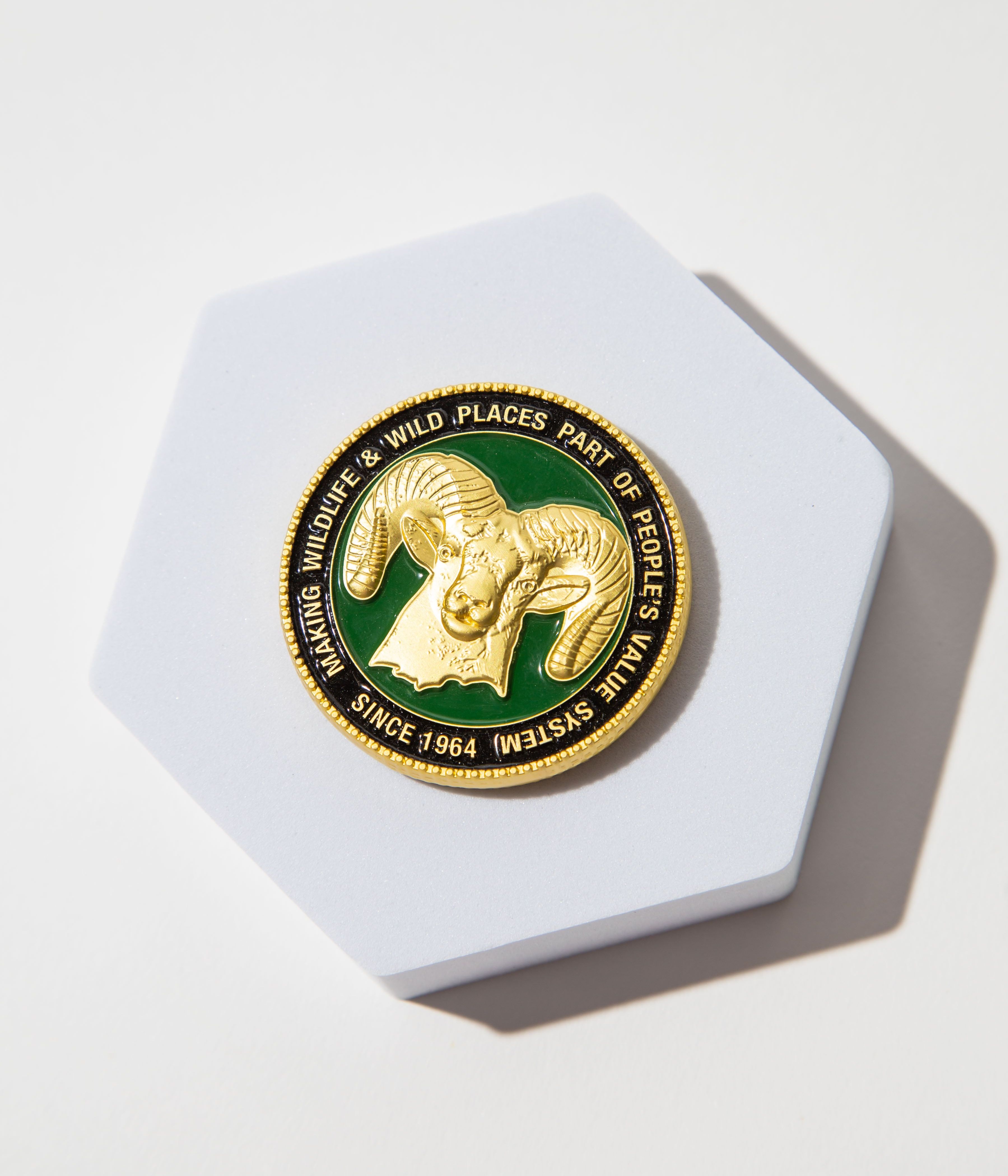 Gold medallion with a ram's head on a green background, promoting wildlife conservation since 1964.