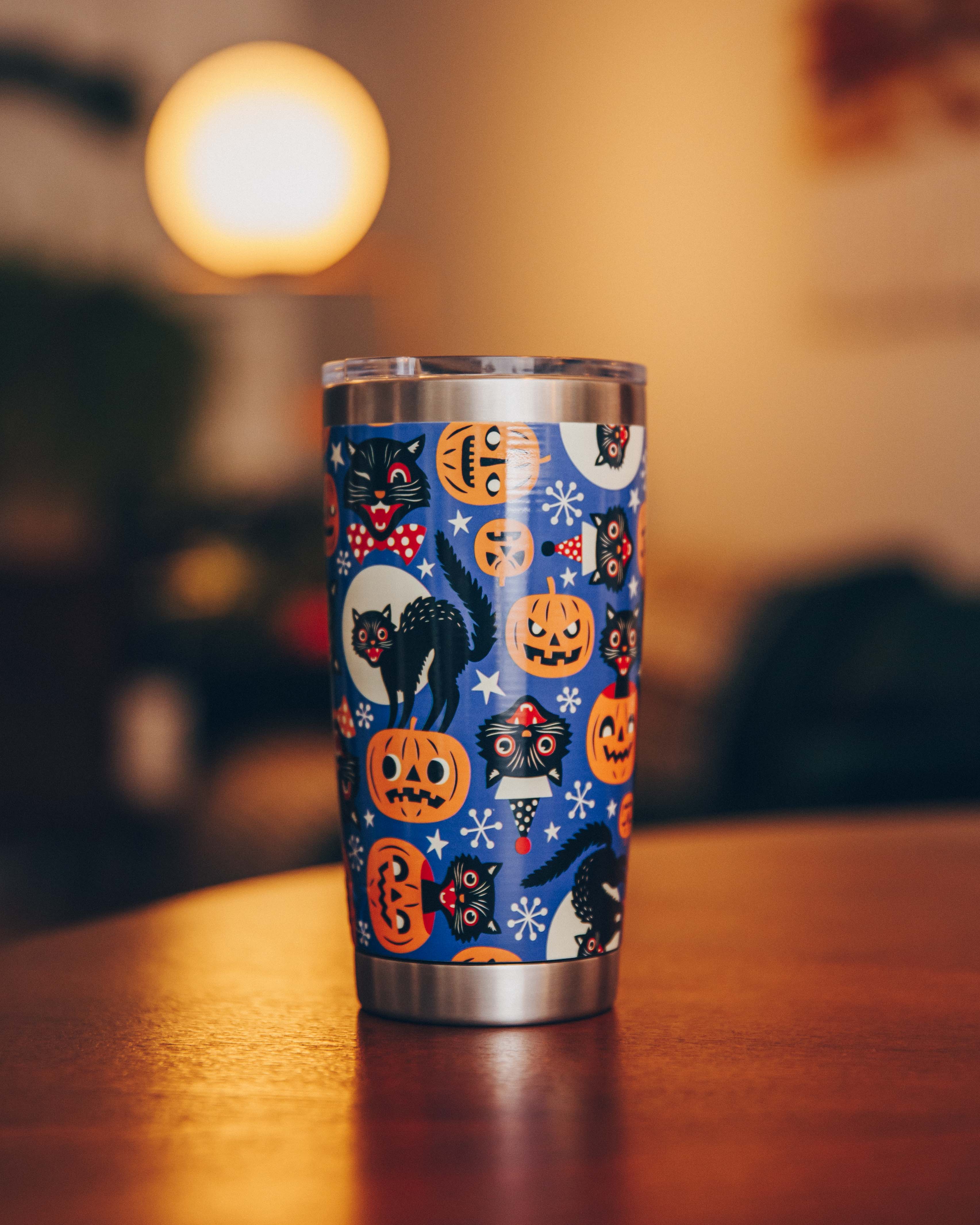 Stainless steel tumbler with Halloween design featuring black cats and pumpkins on a table.