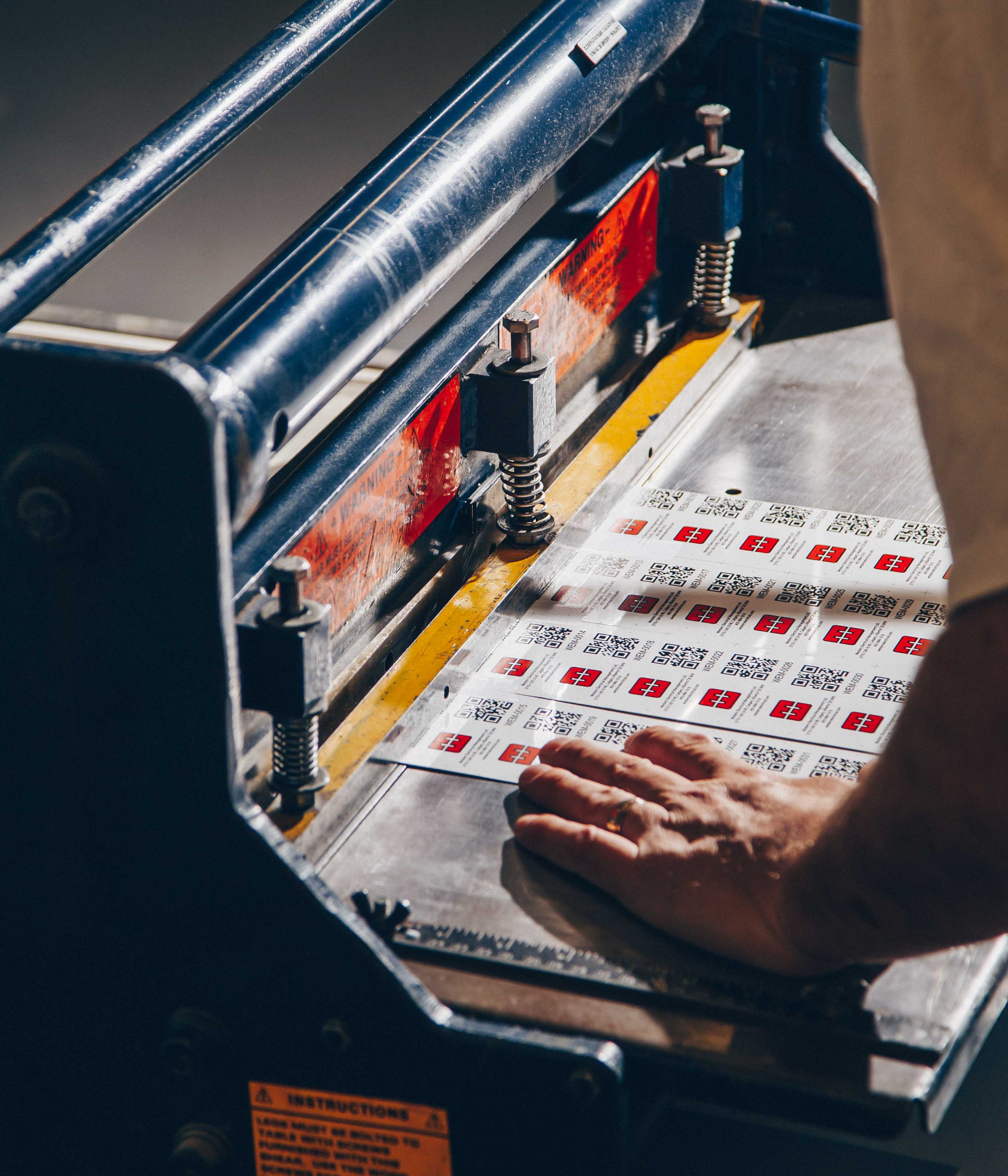 Person using cutting device to split sheet of metal labels apart.