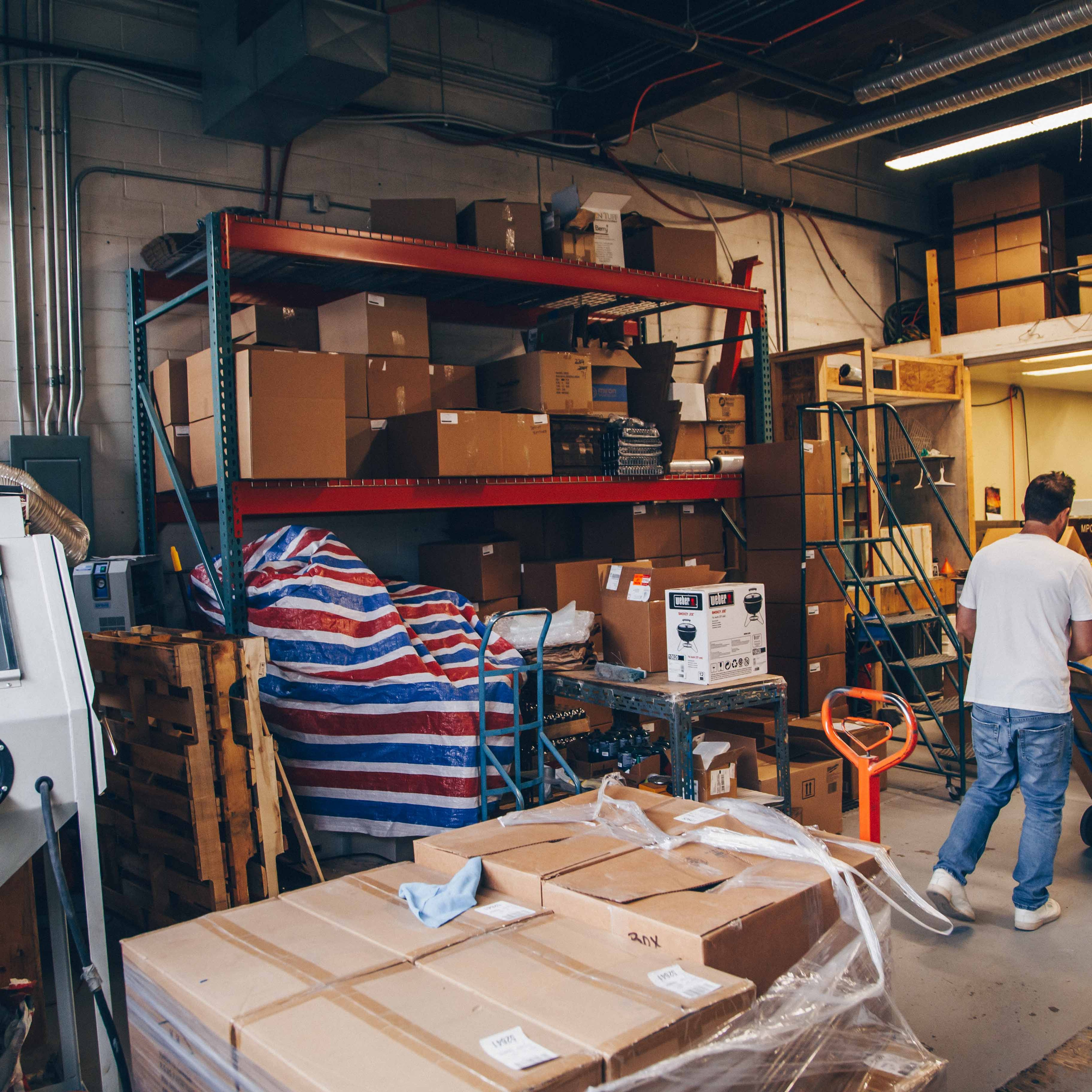 Warehouse workers moving boxes with a hand truck in a cluttered storage area.