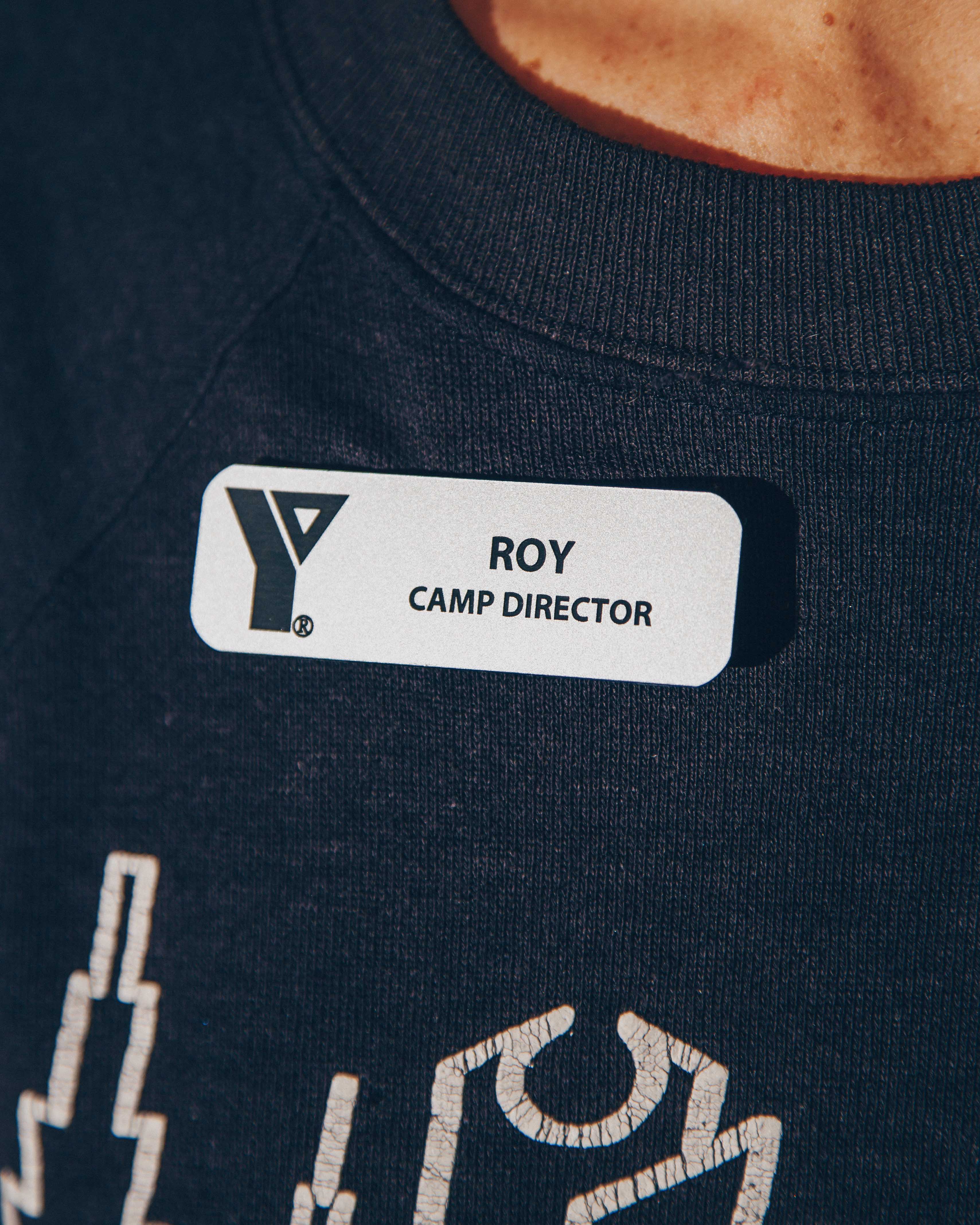 Close-up of a name tag reading 'Roy, Camp Director' on a dark shirt.