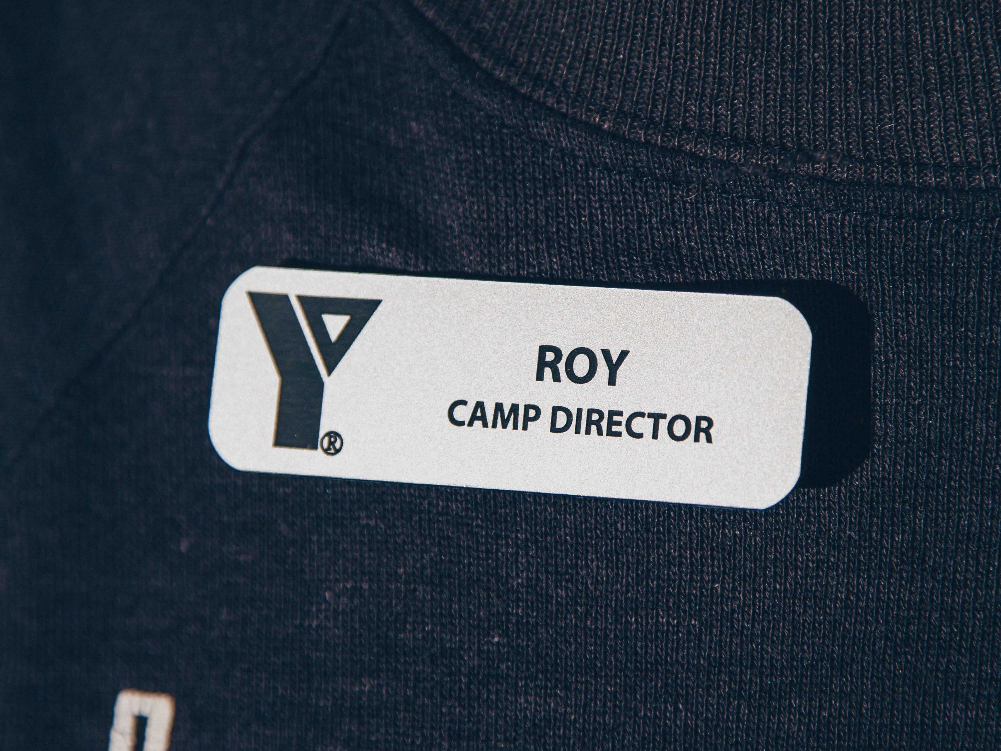 Close-up of a name tag reading 'Roy, Camp Director' on a dark shirt.