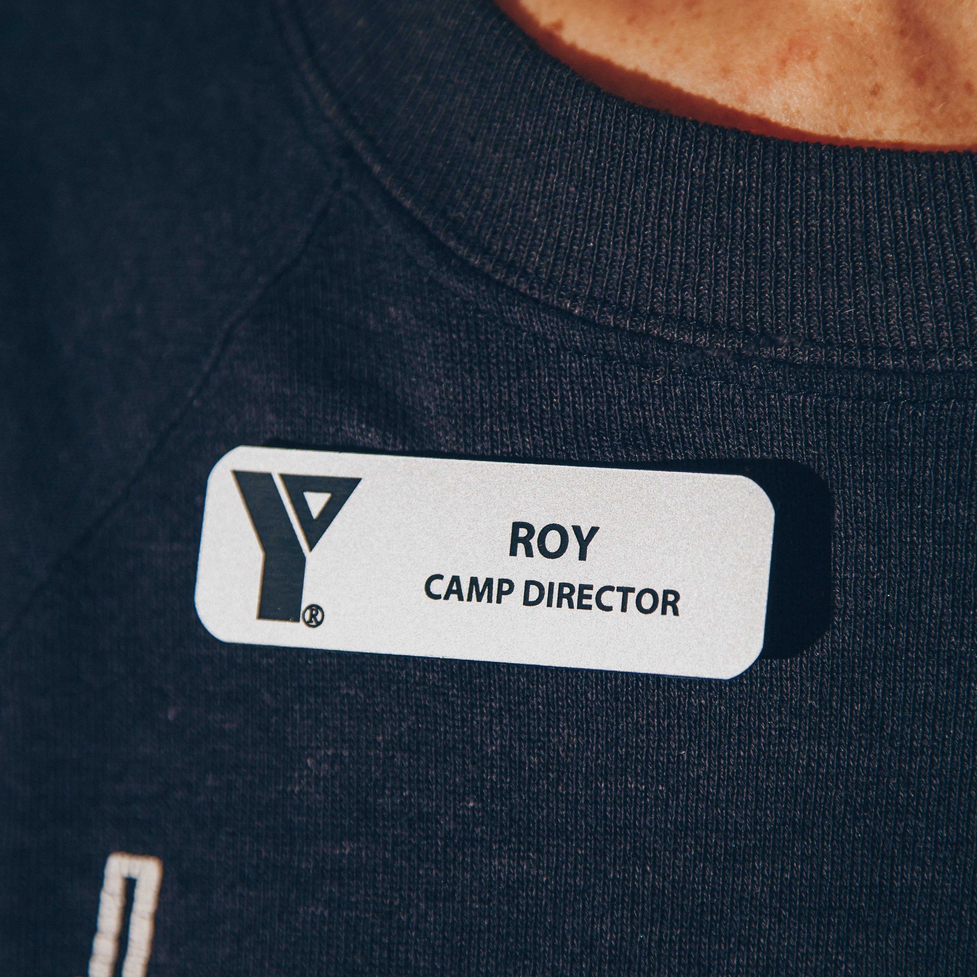 Close-up of a name tag reading 'Roy, Camp Director' on a dark shirt.