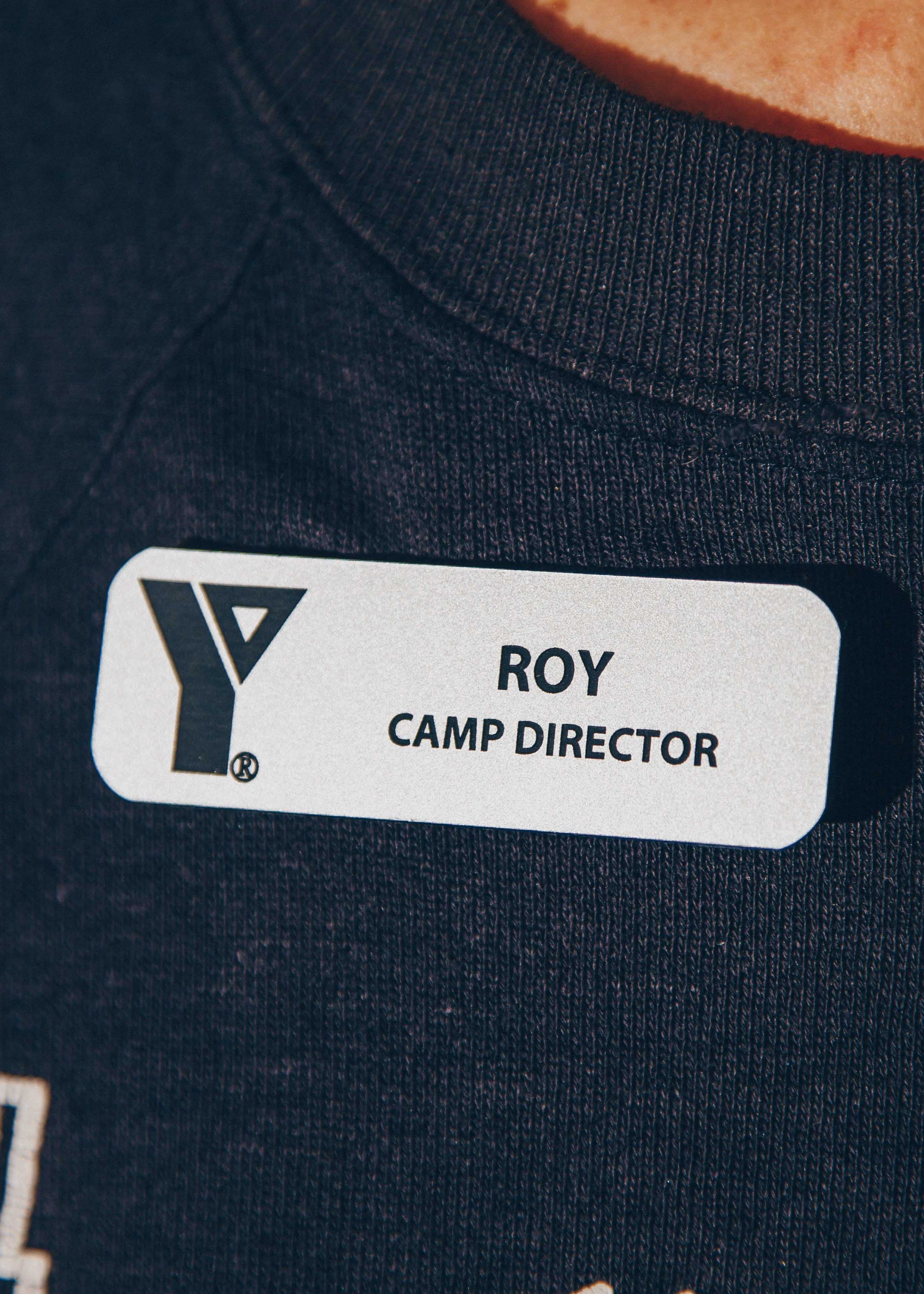 Close-up of a name tag reading 'Roy, Camp Director' on a dark shirt.