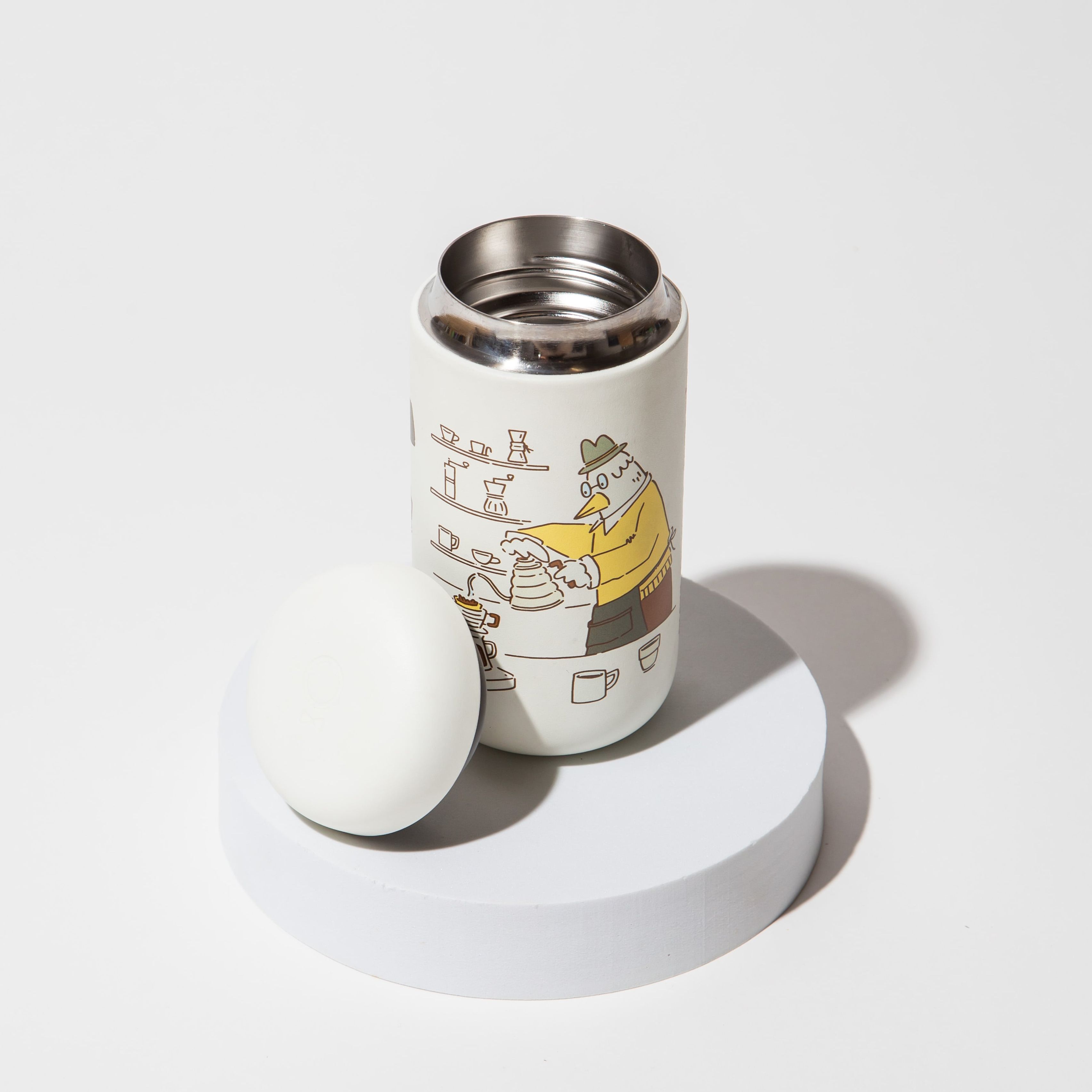 White thermos with cartoon illustration on a round pedestal, lid removed.