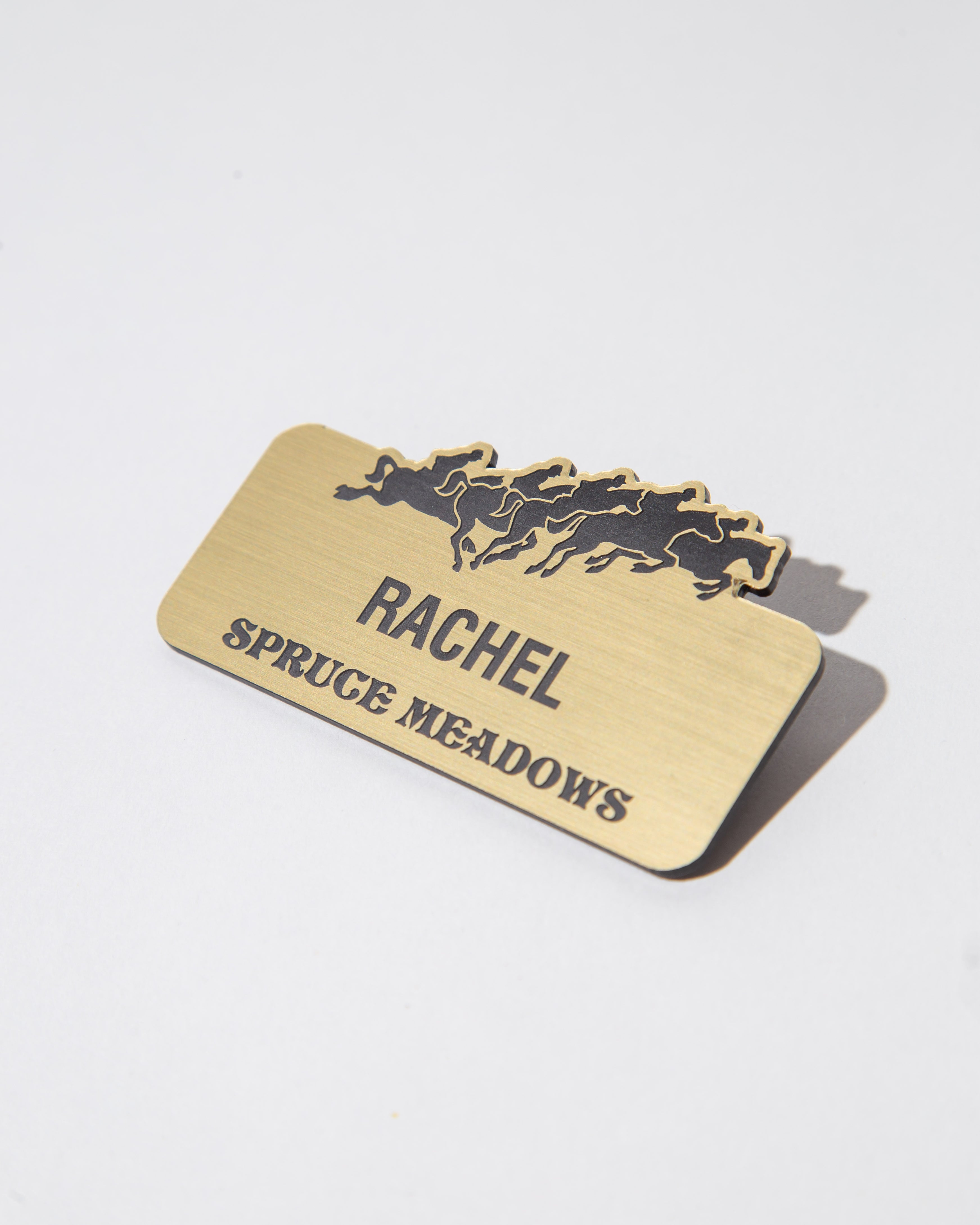 Brass name tag with horse silhouettes and the name 'Rachel' above 'Spruce Meadows'.