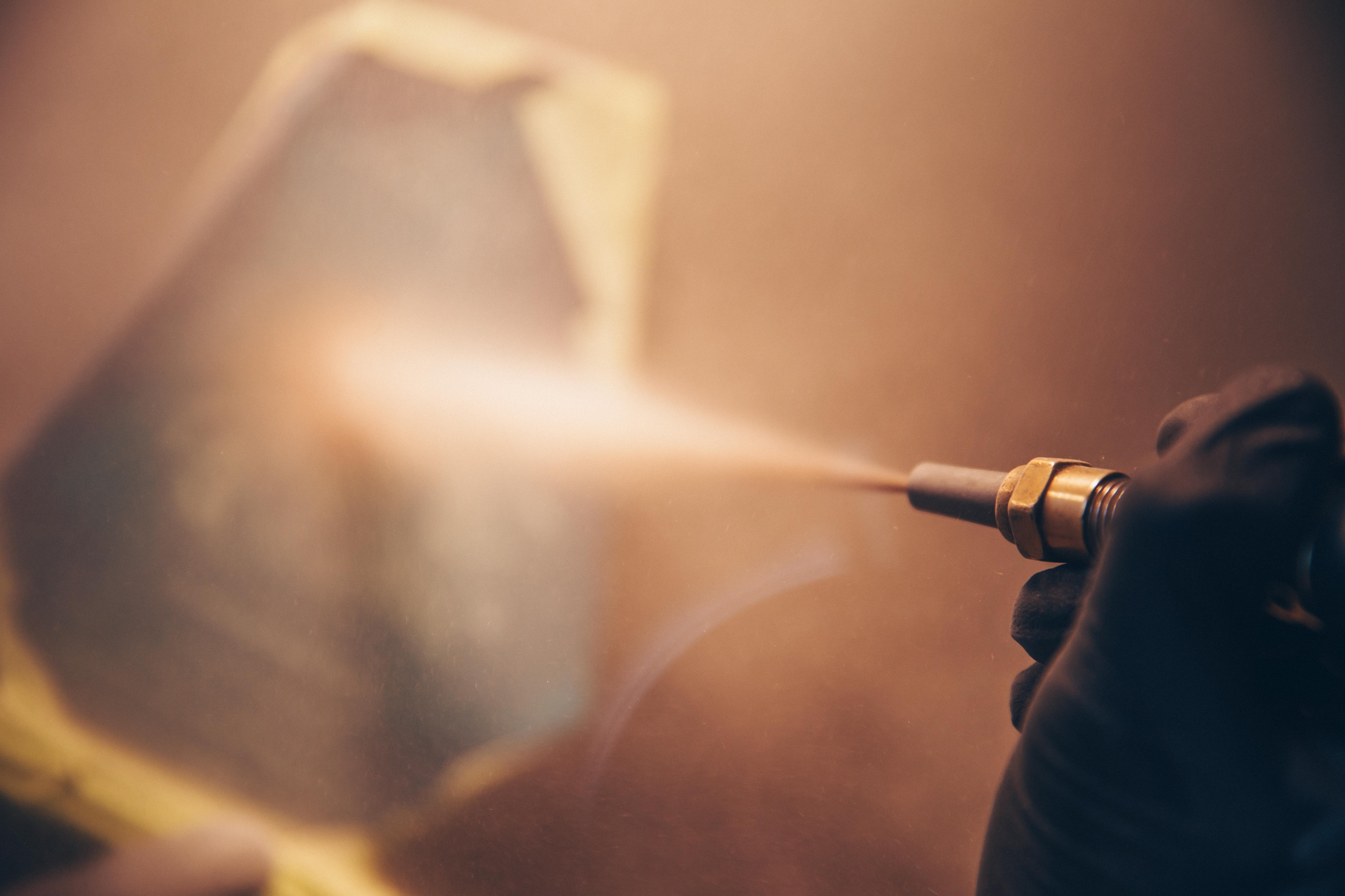 Close-up of a sandblasting nozzle spraying fine material onto a glass surface, creating detailed engravings for a custom award or trophy.