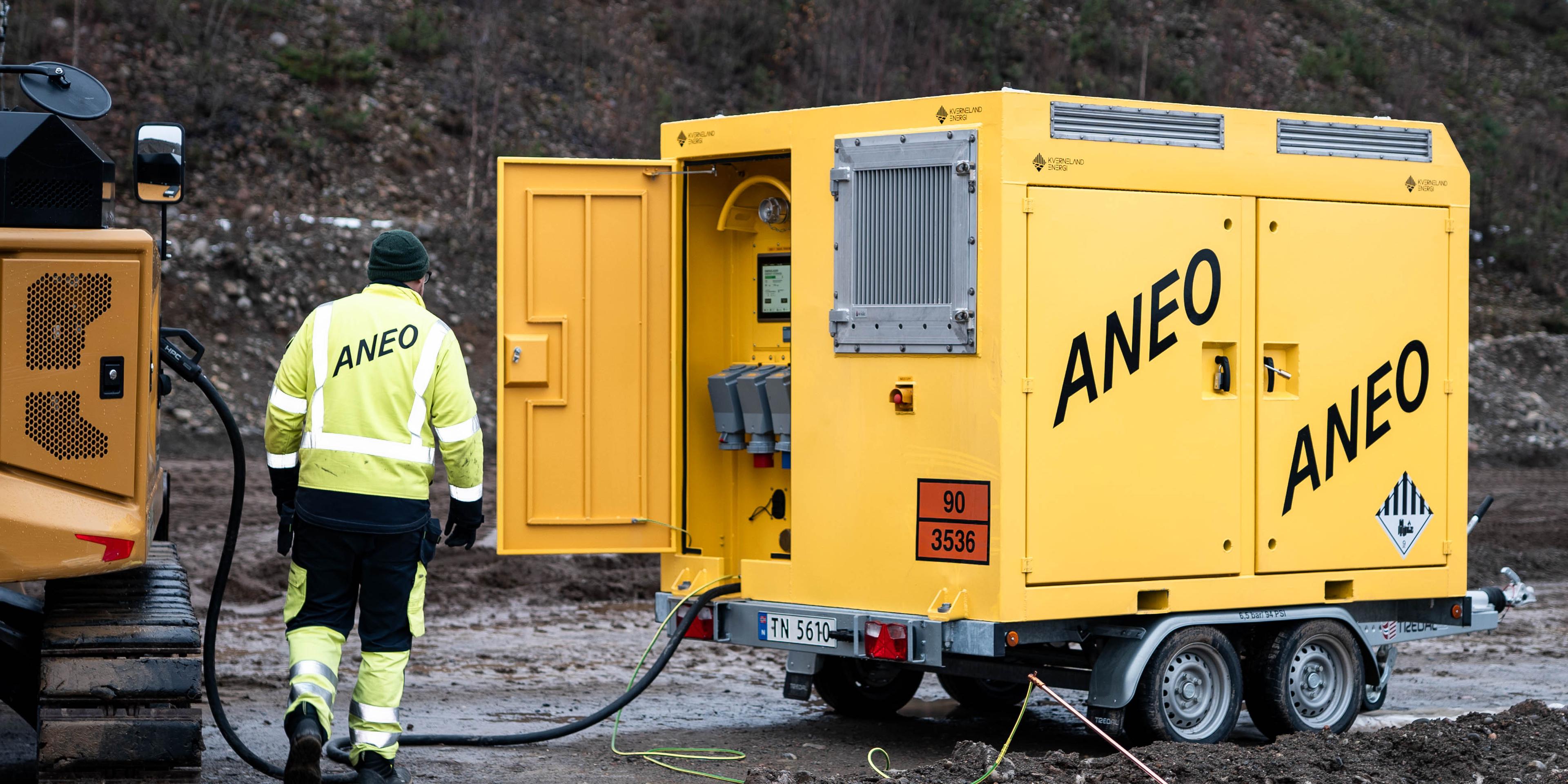 en mann i gul jakke og svarte bukser som står ved siden av en mobil strømenhet