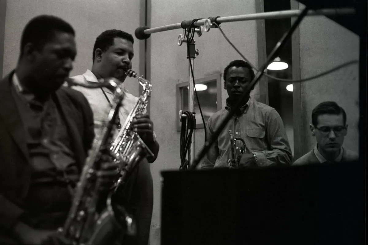 John Coltrane y Cannonball Adderley aparecen en primer término con sus saxofones; tras ellos, Miles Davis posa con su trompeta cerca de Bill Evans, quien se encuentra al piano.