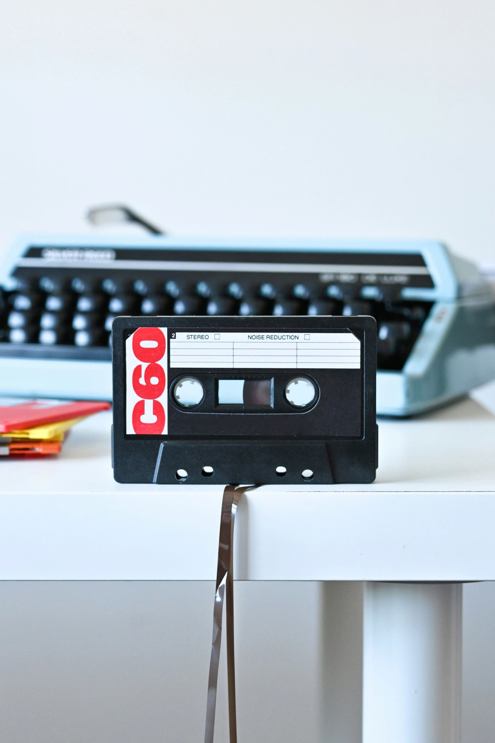 Een cassettebandje rechtop voor een vintage typemachine, met de band die uit het cassettebandje loopt.