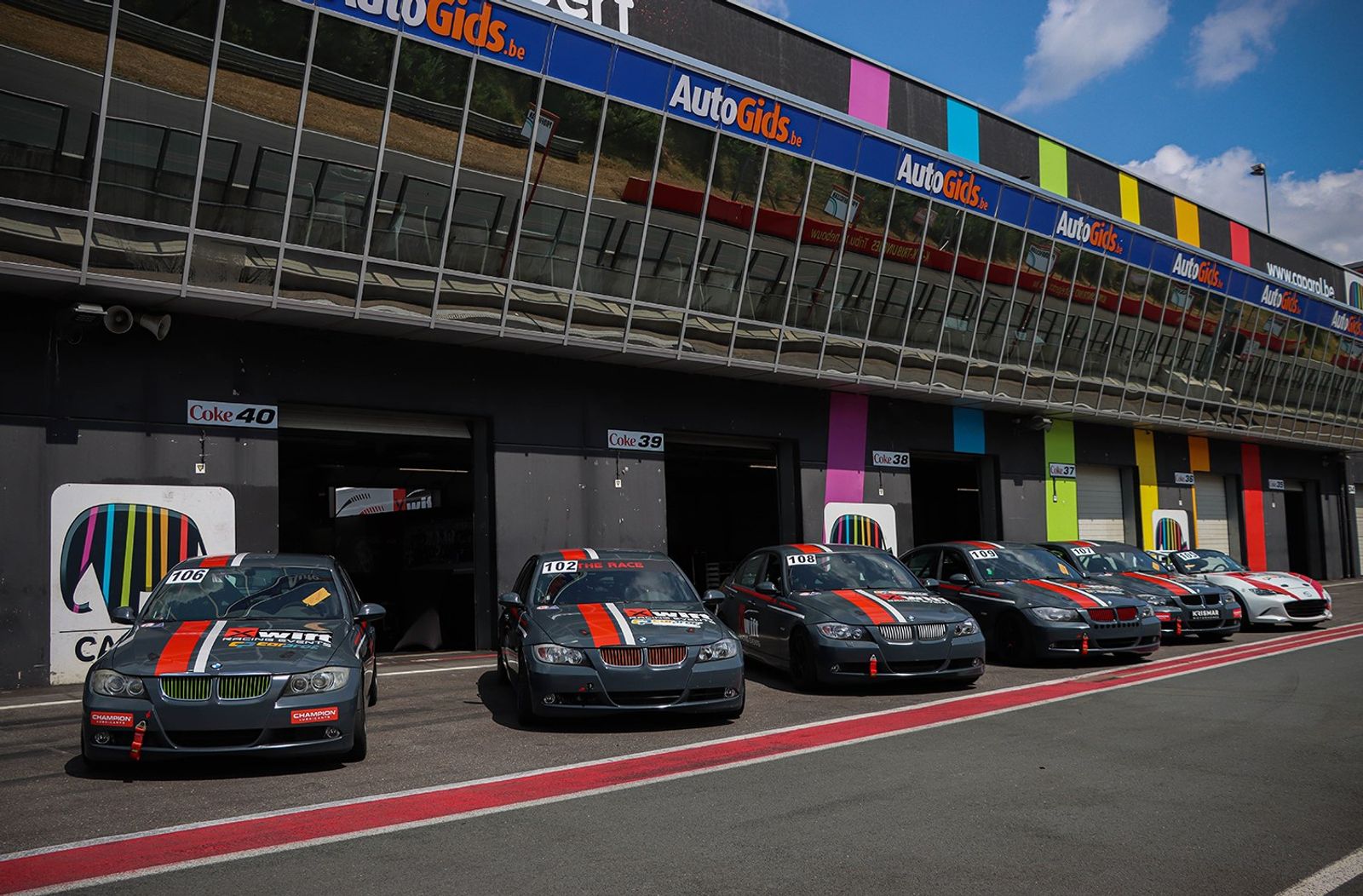 Een rij BMW's van Xwift Racing in teamkleuren in de pitstraat voor de garages.