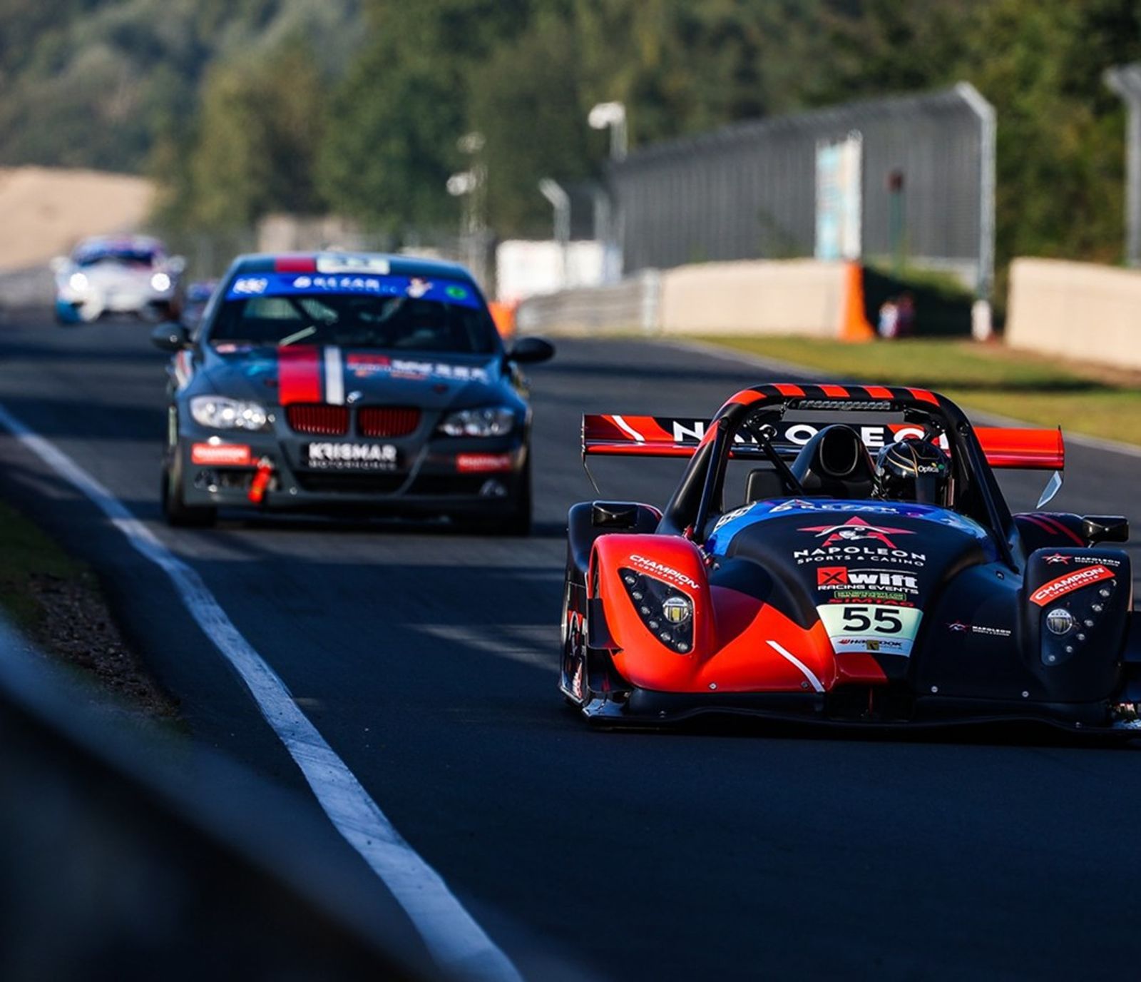 Een Radical-racewagen met nummer 55 rijdt voor een BMW uit op het rechte stuk.