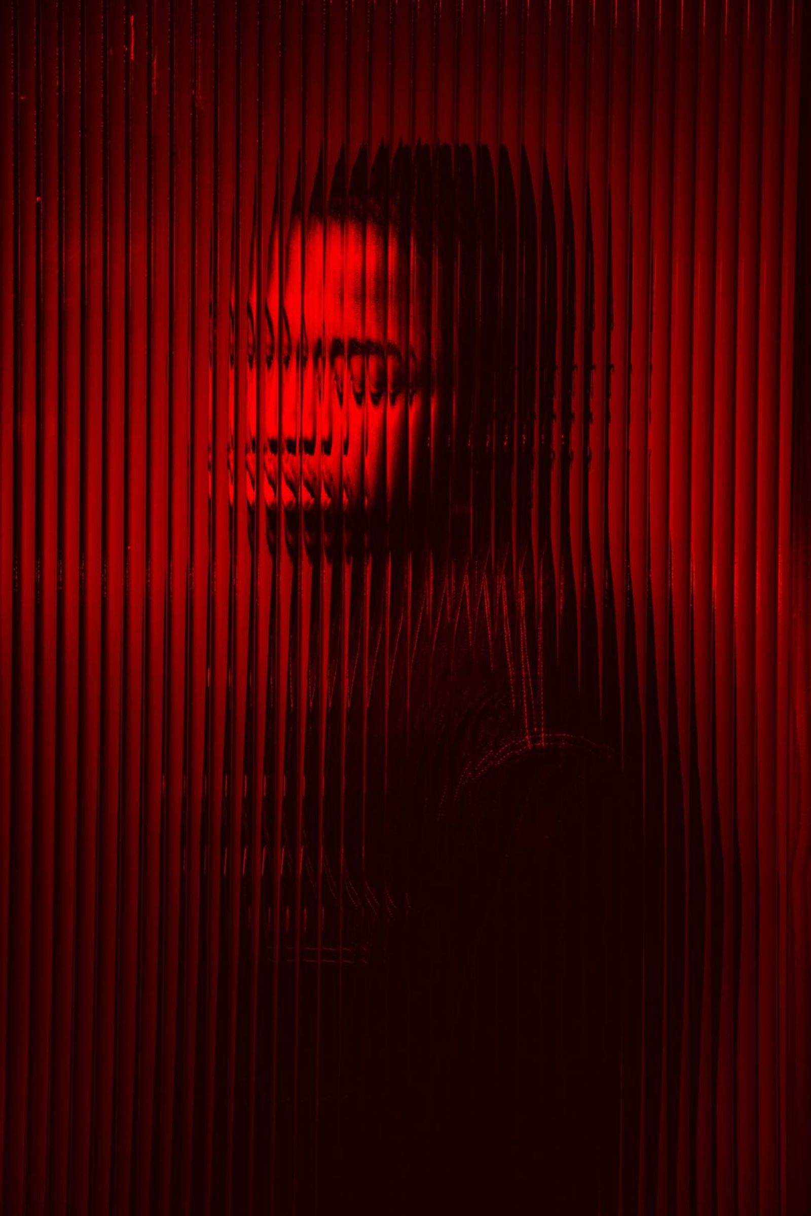 A portrait seen through fluted glass in deep red light.