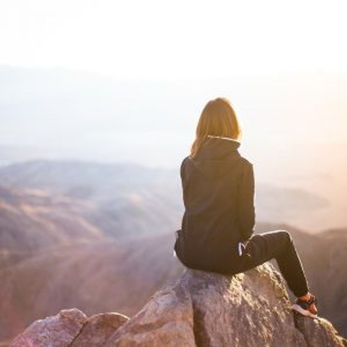 Frau die auf einem Berggipfel sitzt und von hinten zu sehen ist als Zeichen für das Gefühl der Verbundenheit in der Welt