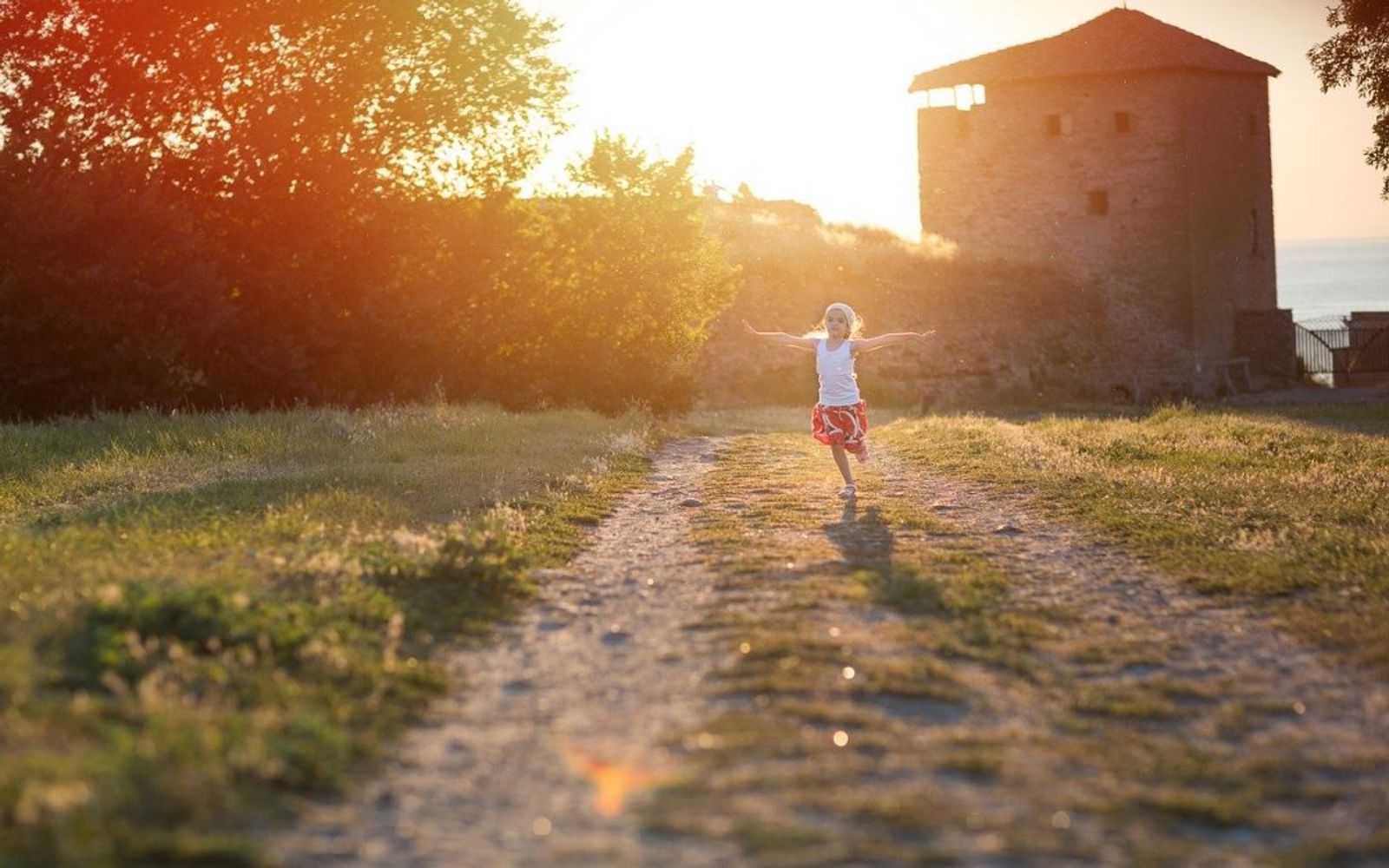 Kleines Mädchen hüpft im Sonnenuntergang auf einem Weg auf der Wiese
