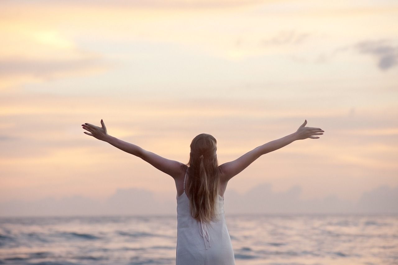 Frau mit offenen Armen am Meer als Sinnbild für Freude an Meditation