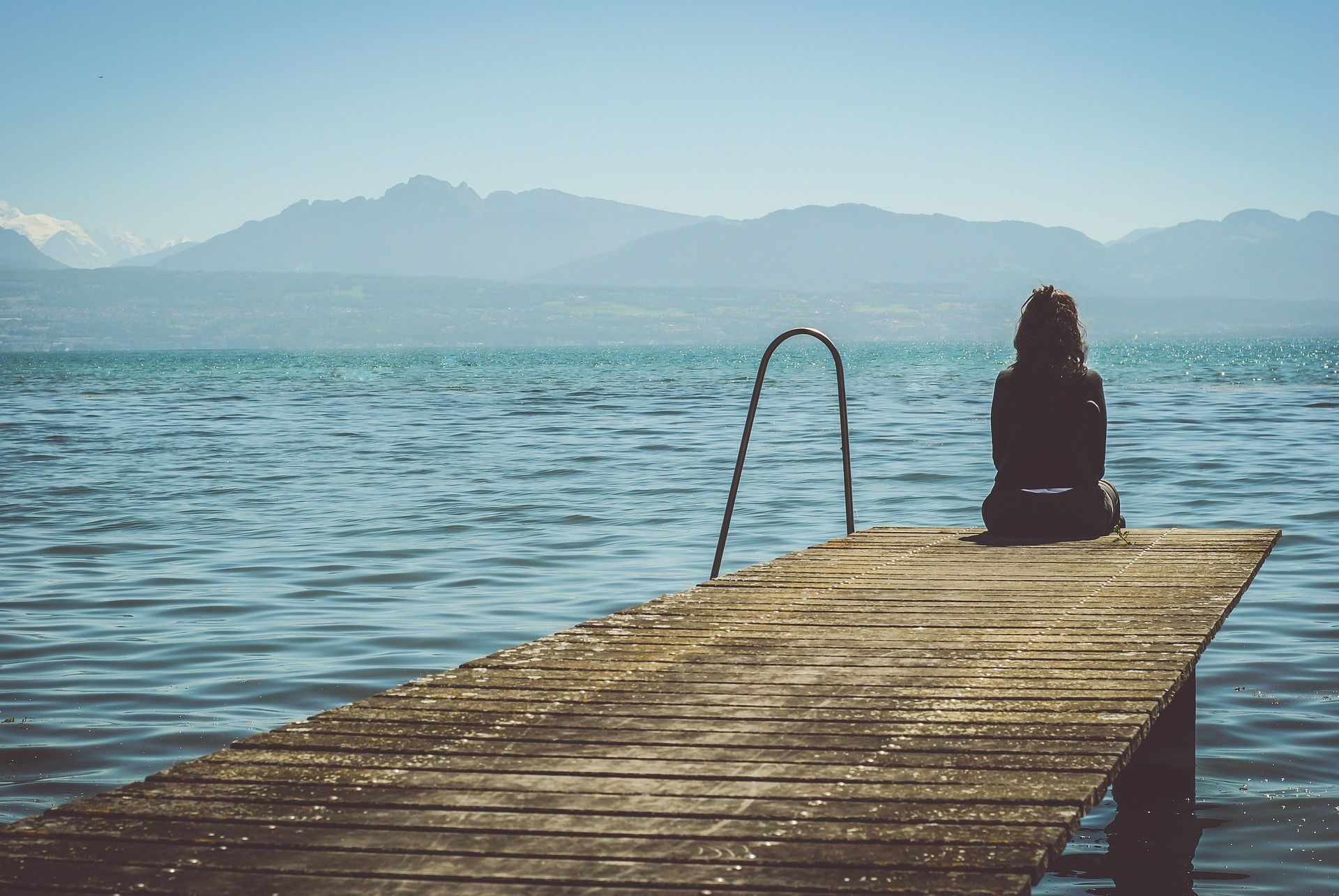 Frau sitzt auf einem Steg am Wasser, schaut ruhig in die Berge als Sinnbild dafür, wie man seine Depression überwinden kann