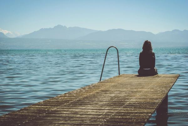 Frau sitzt auf einem Steg am Wasser, schaut ruhig in die Berge als Sinnbild dafür, wie man seine Depression überwinden kann