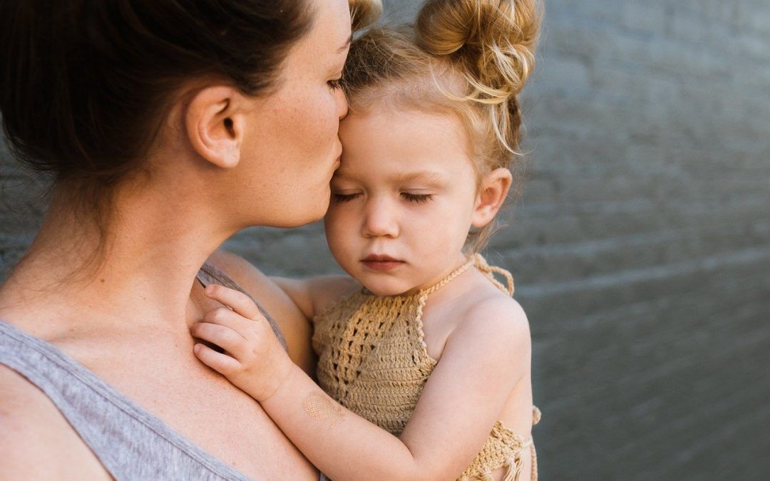 Mutter hält kleine Tochter auf dem Arm und gibt ihr einen Kuss