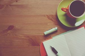 Stift und Notizbuch auf einem Tisch und ein halb sichtbare Kaffeetasse