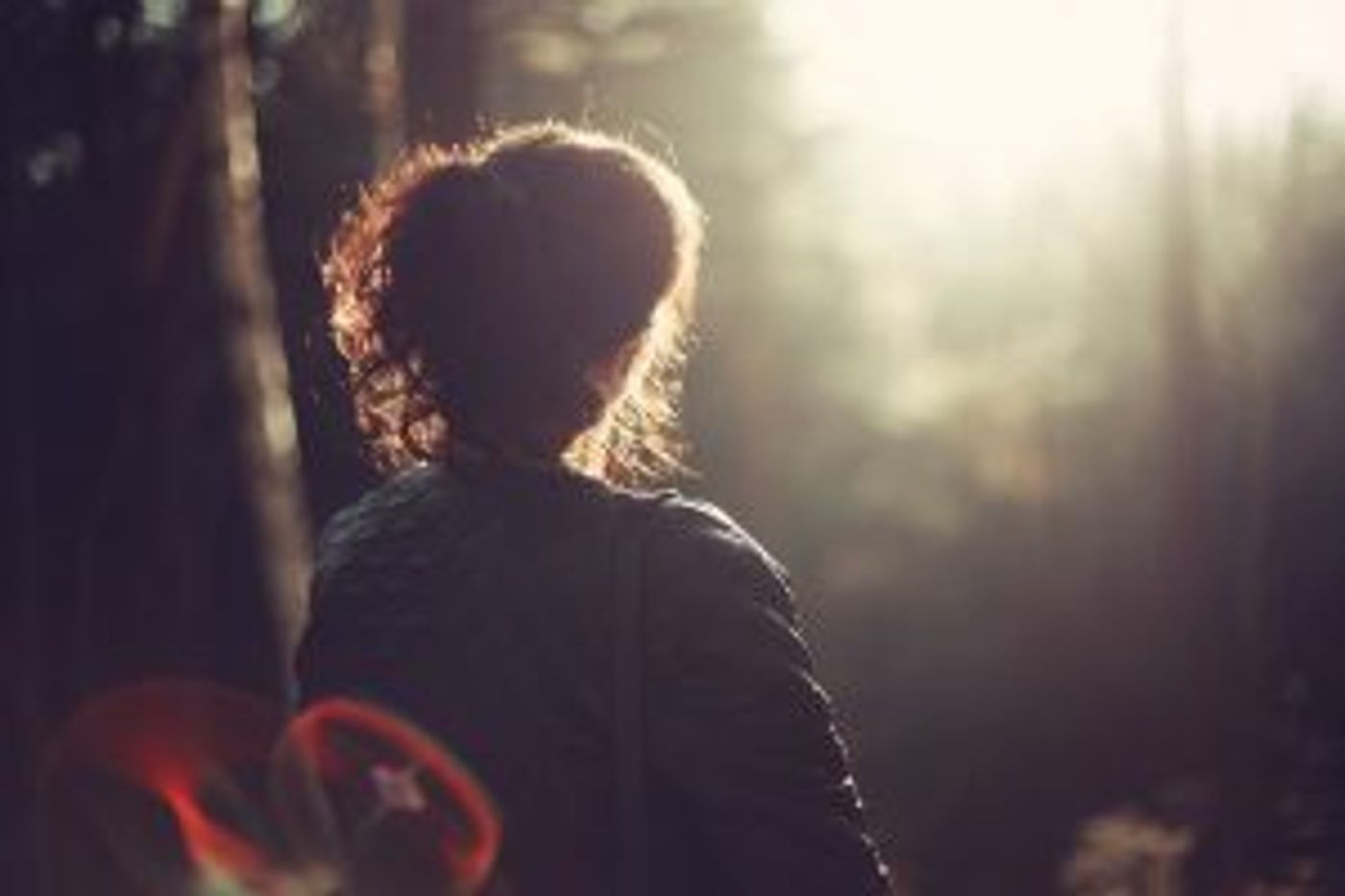 Frau im Wald von hinten sichtbar im sanften Licht 