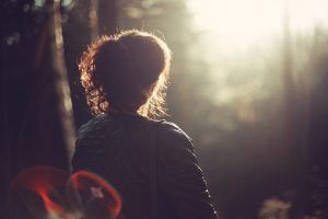Frau im Wald von hinten sichtbar im sanften Licht