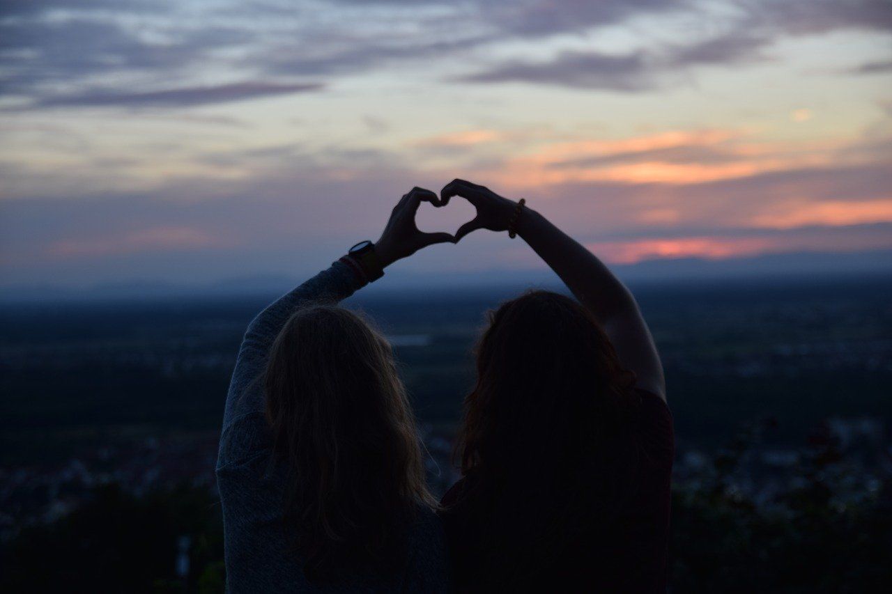 Zwei Mädchen halten ihre Hände als Herz gemeinsam in den dunklen Abendhimmel