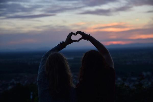 Zwei Mädchen halten ihre Hände als Herz gemeinsam in den dunklen Abendhimmel