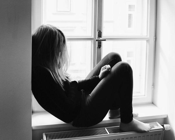 Frau sitzt zusammengesunken im Fenster als Sinnbild für den Schmerz von Trauma