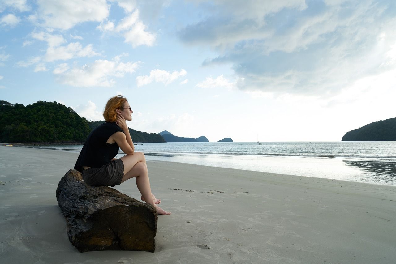 Frau sitzt auf einem Baumstamm am Meer