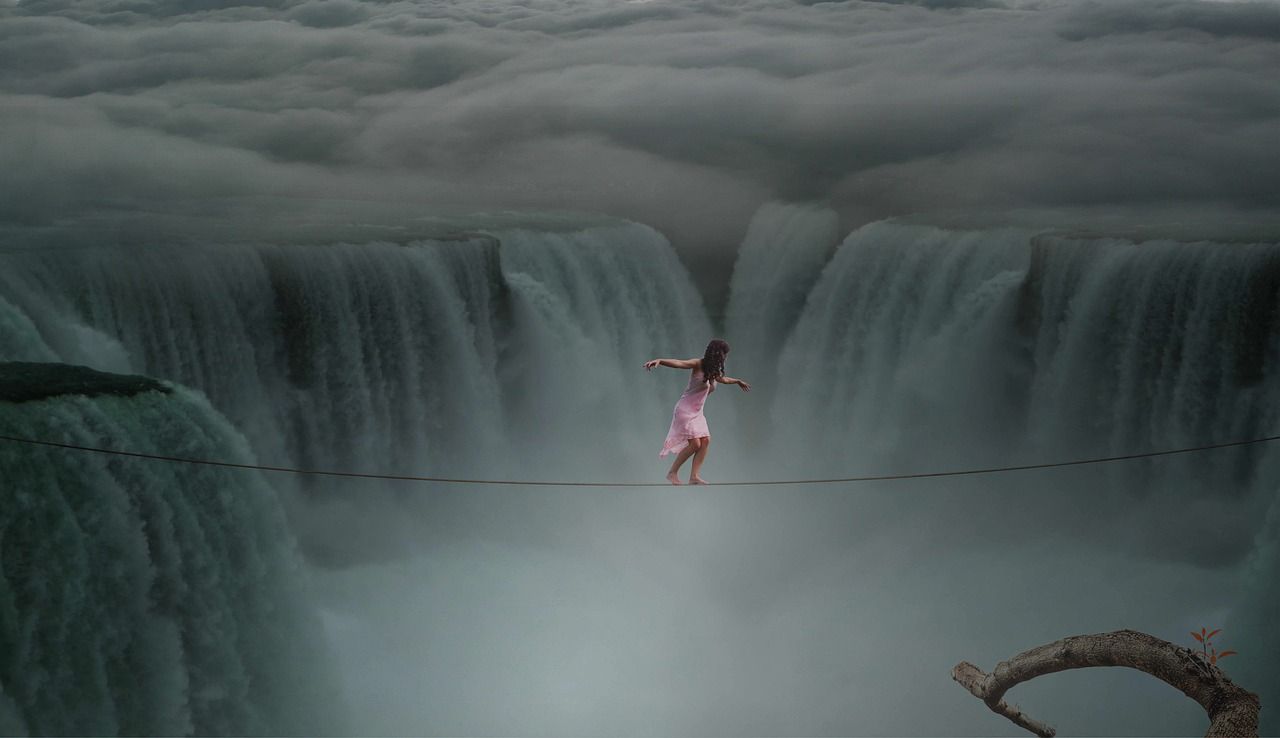 Frau auf einen Drahtseil über einem Wasserfall als Sinnbild für eine Krise