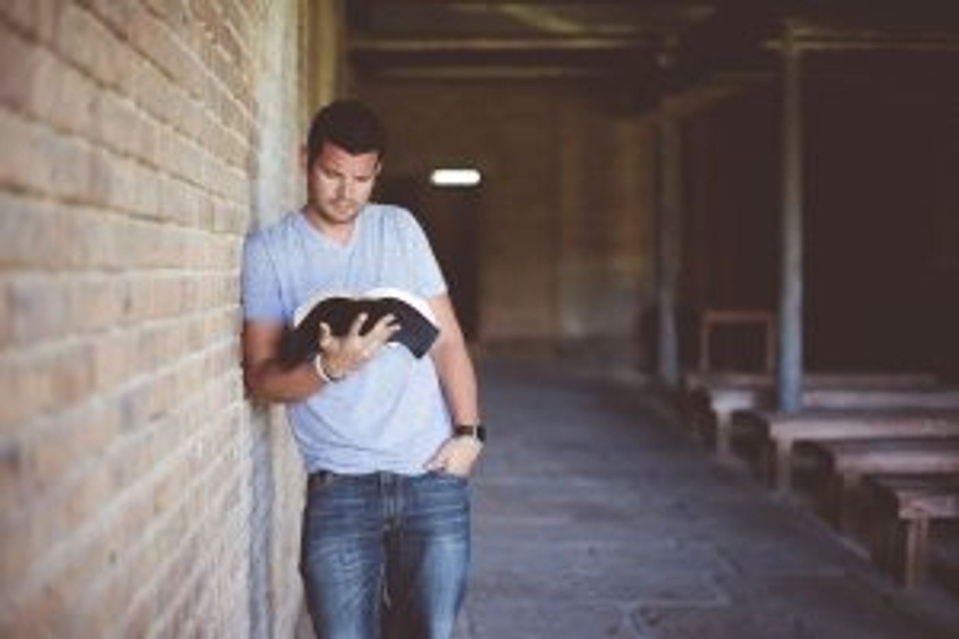 Mann lehnt an einer Mauer und liest in einem Buch
