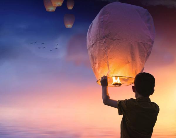 Junge der ein Licht in den Himmel aufsteigen lässt als Sinnbild für das Loslassen