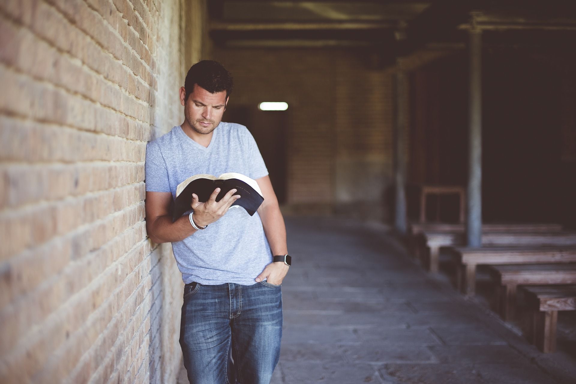 Mann lehnt an einer Mauer und liest in einem Buch