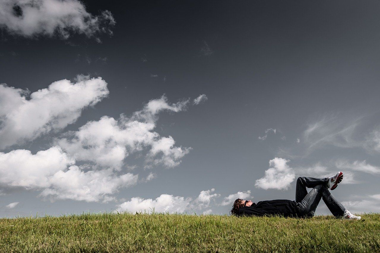 Mann liegt im Gras und schaut in die Wolken als Sinnbild für eigene Träume und die Löffelliste
