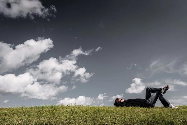 Mann liegt im Gras und schaut in die Wolken als Sinnbild für eigene Träume und die Löffelliste