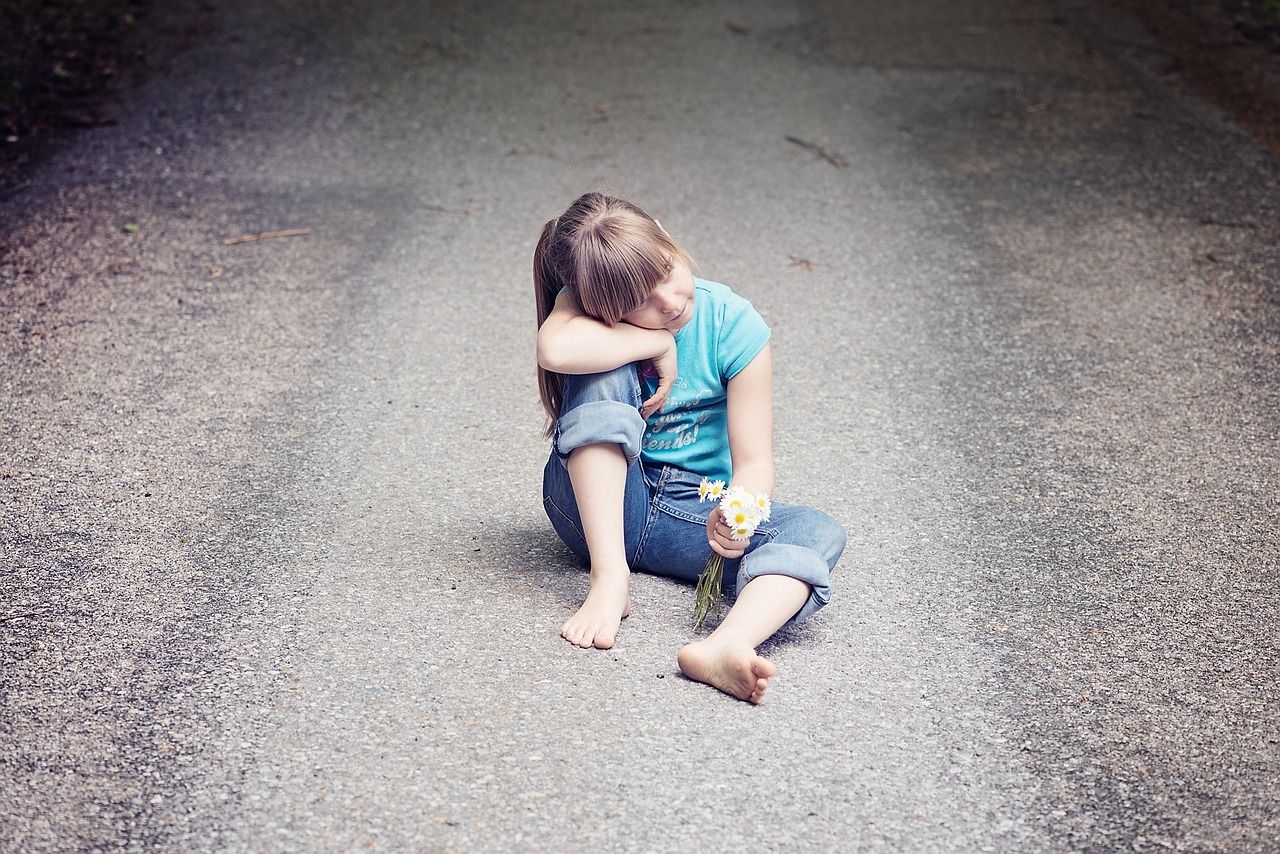Kleines Mädchen sitzt auf einer Straße mit Blumen in der Hand als Sinnbild für unser inneres Kind